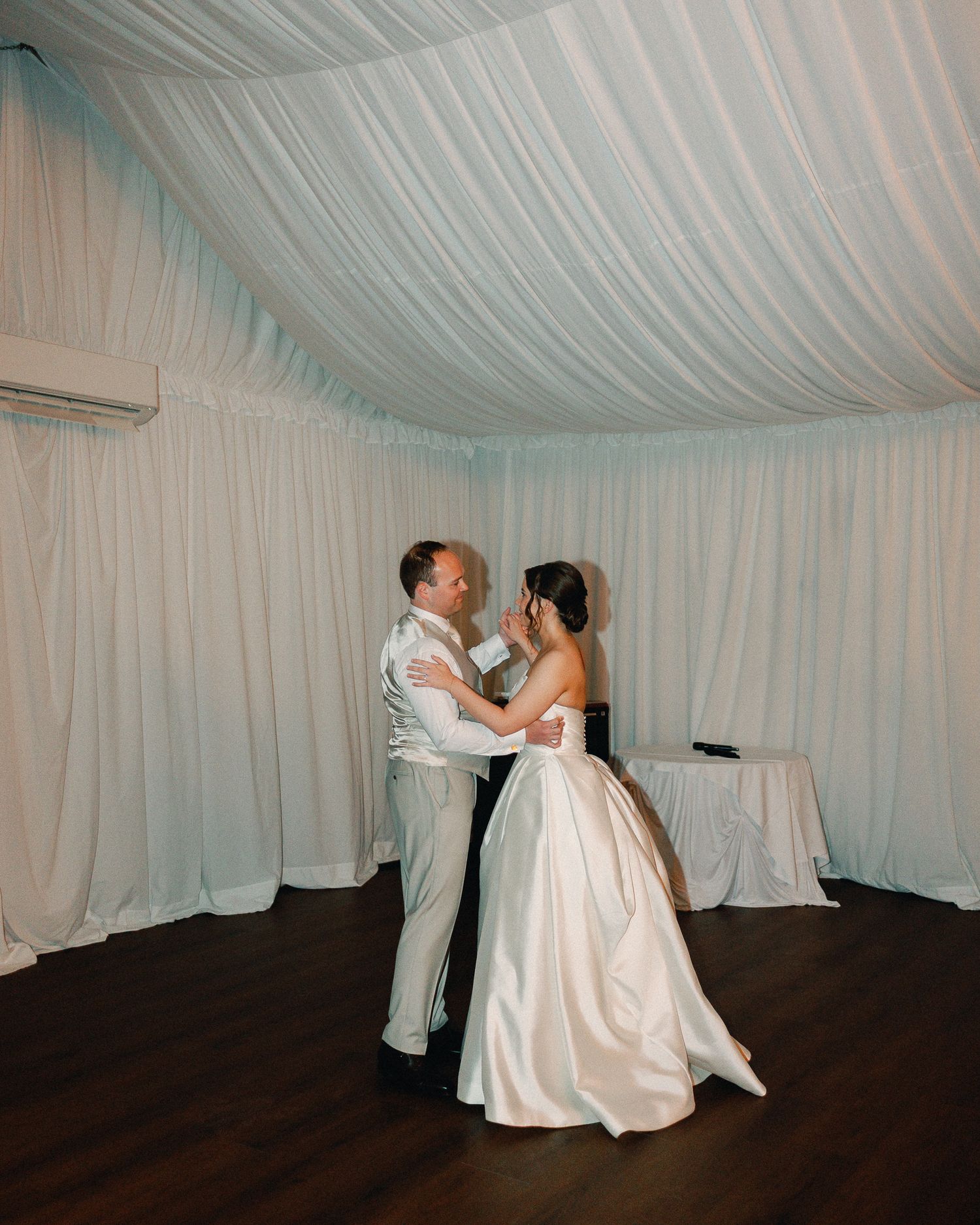 Bride and groom share their first dance under elegant white draped ceiling at wedding reception.