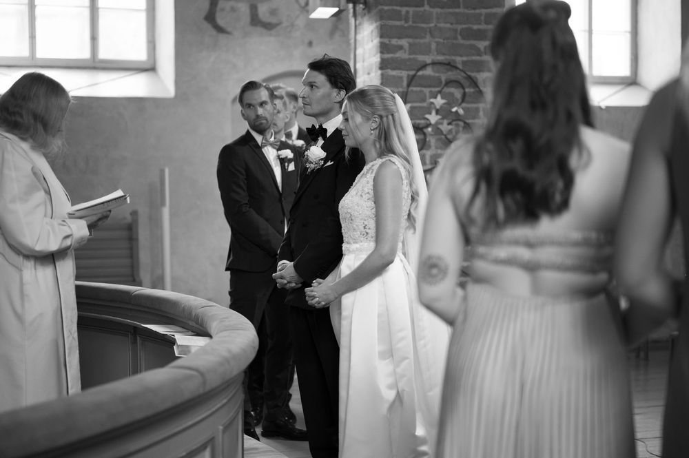 Wedding party standing in a historic church with exposed brick walls and windows.