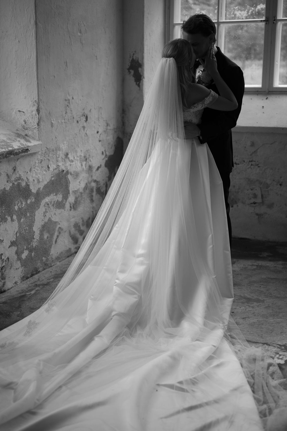 A romantic black and white wedding photo showing a couple embracing with the bride's long flowing veil trailing behind.