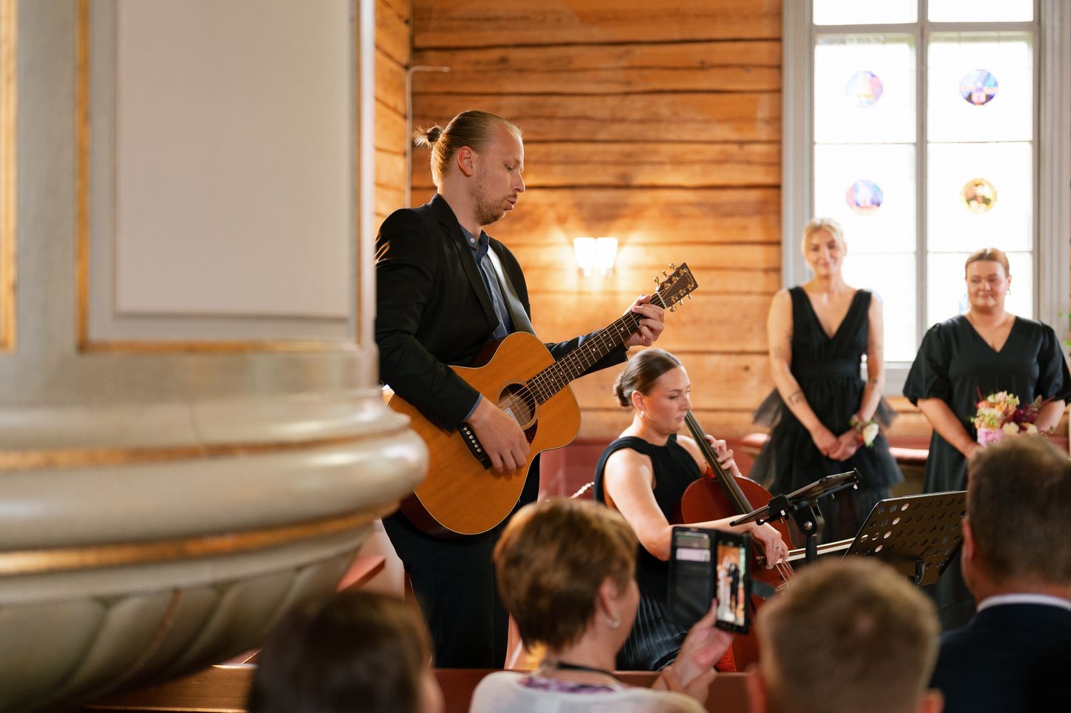 Musicians perform live music during a rustic wedding ceremony in a wooden cabin venue with natural lighting.