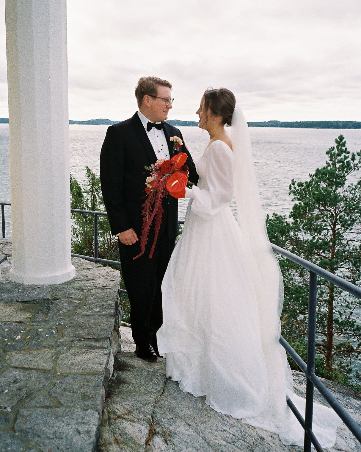 Wedding couple standing on stone terrace overlooking water and coastline.