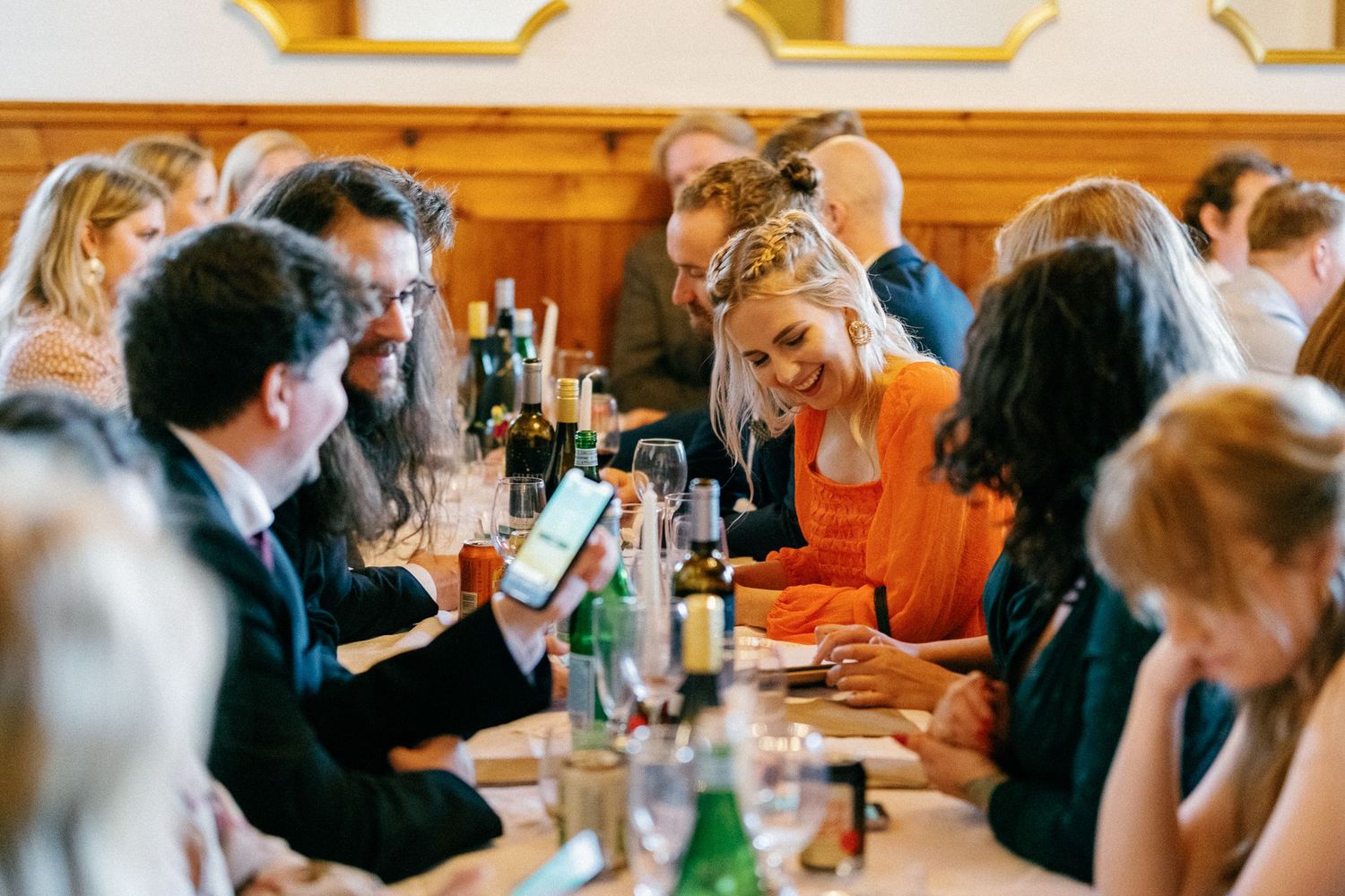 Wedding reception guests mingling in a warm wood-paneled venue with natural lighting.