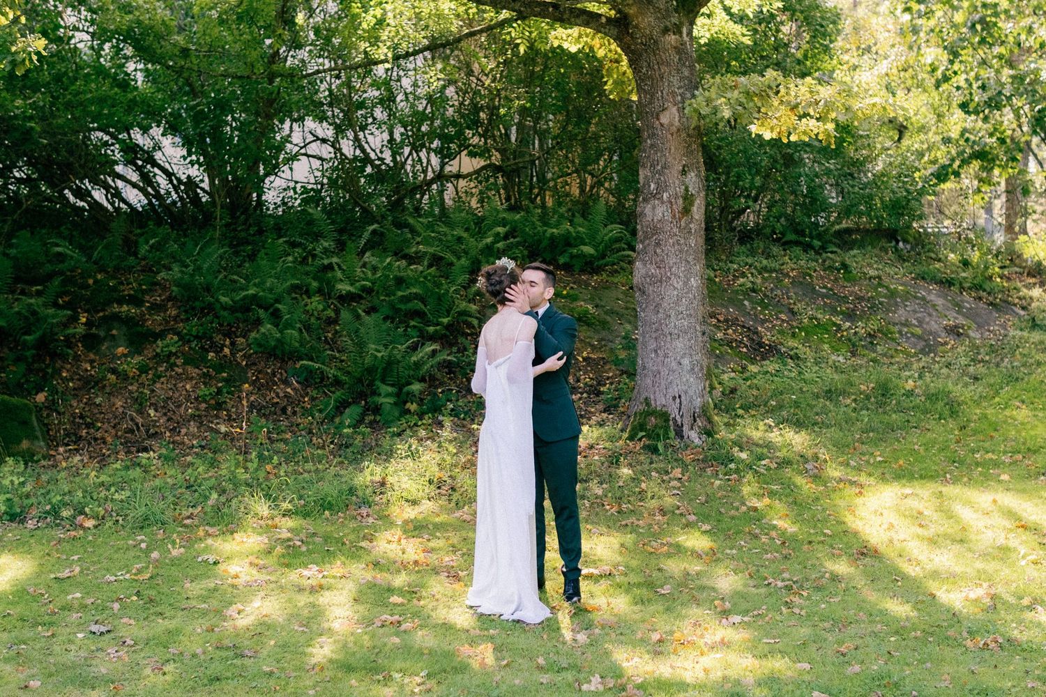 Romantic wedding portraits taken in a sunlit garden with tall trees.