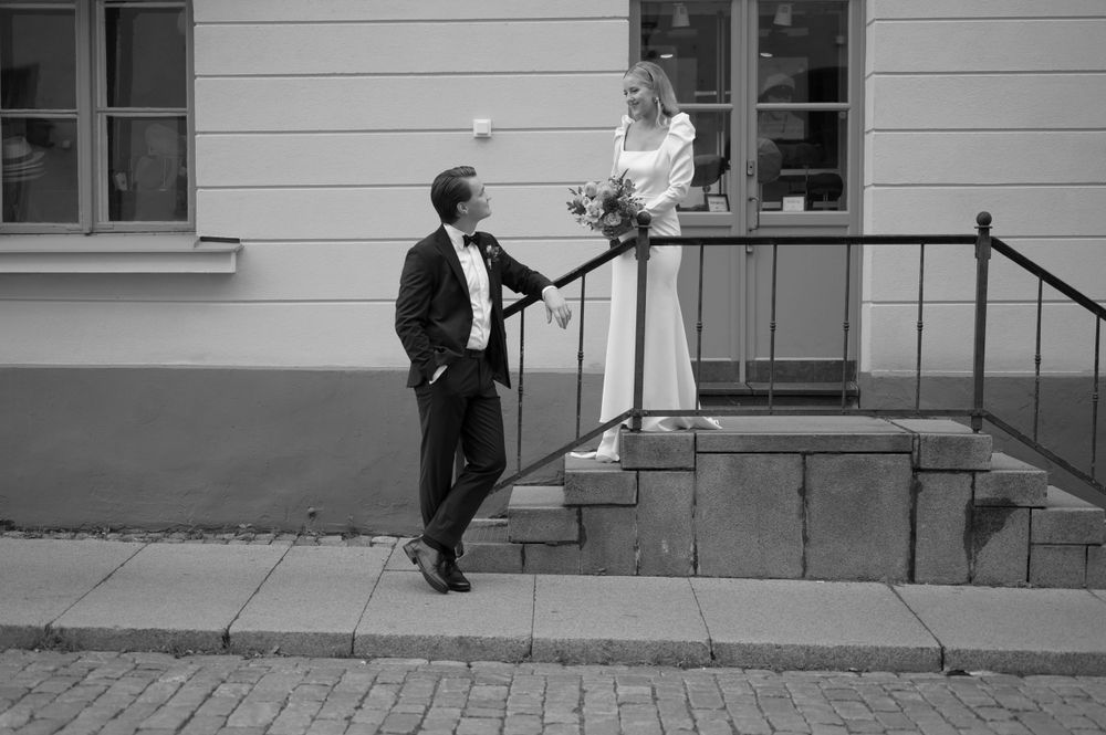 A black and white wedding photo on steps with classic architecture in the background.