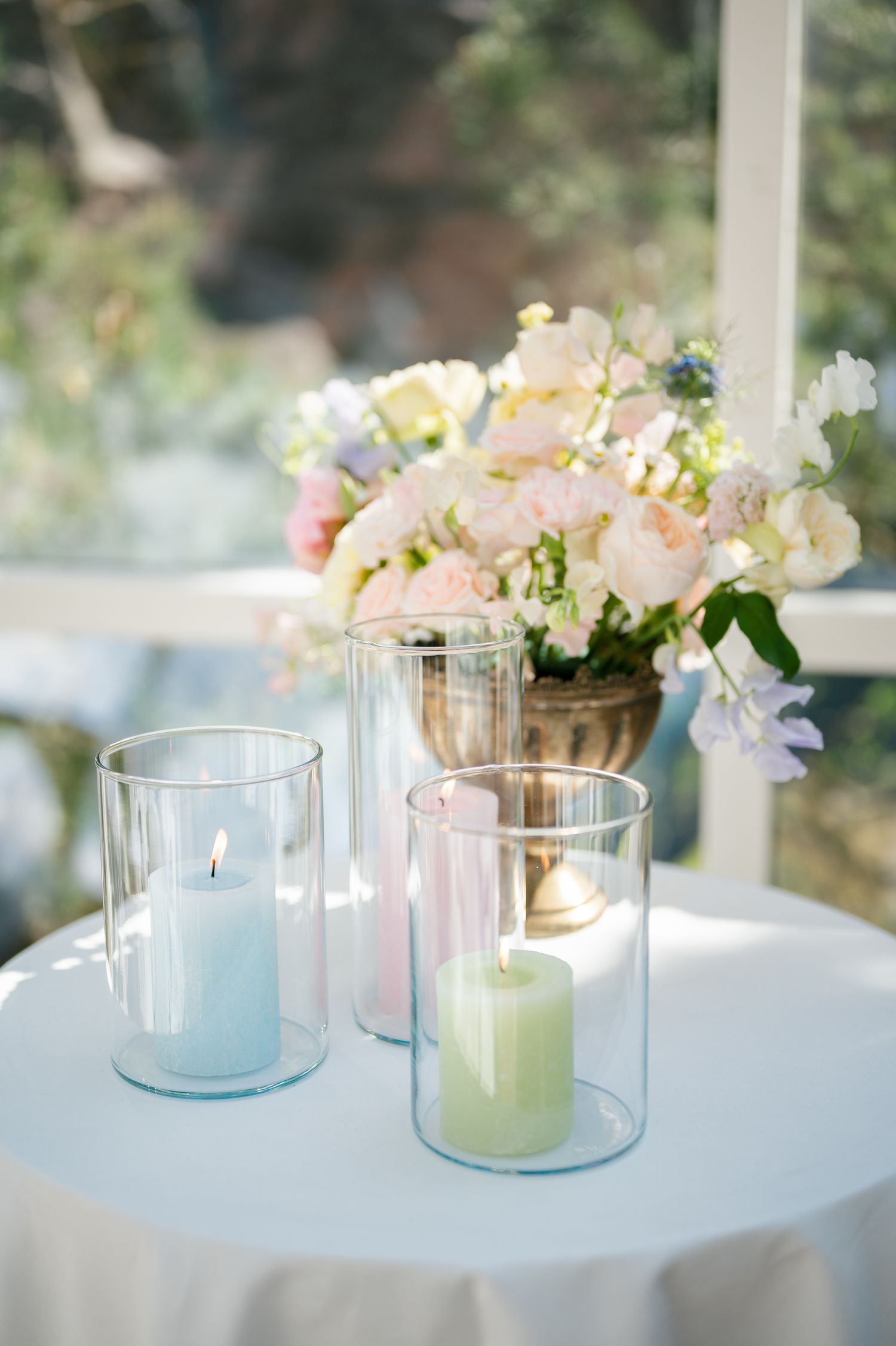 Elegant wedding table with pastel candles in glass holders and a pink floral arrangement in a gold vase.
