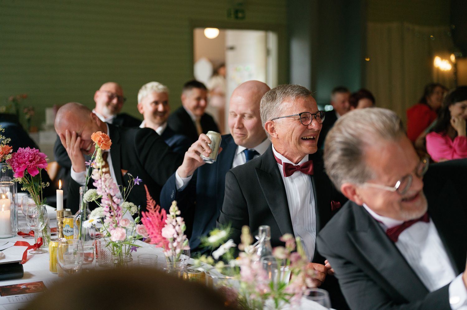 Wedding guests in formal attire enjoying lively conversation at a reception dinner table.