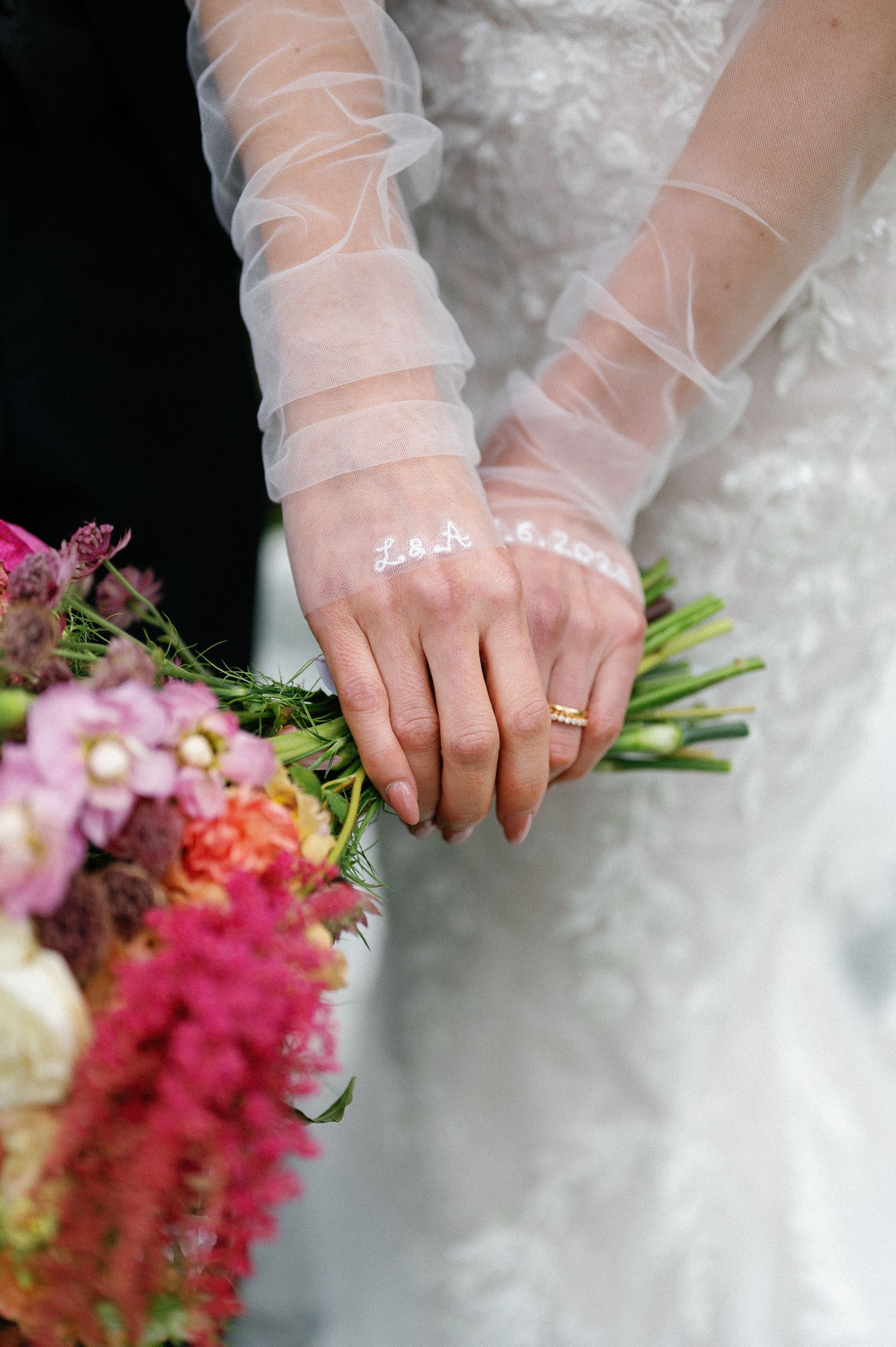 Close-up of bride's hands in sheer gloves holding a colorful bouquet with engagement ring visible.