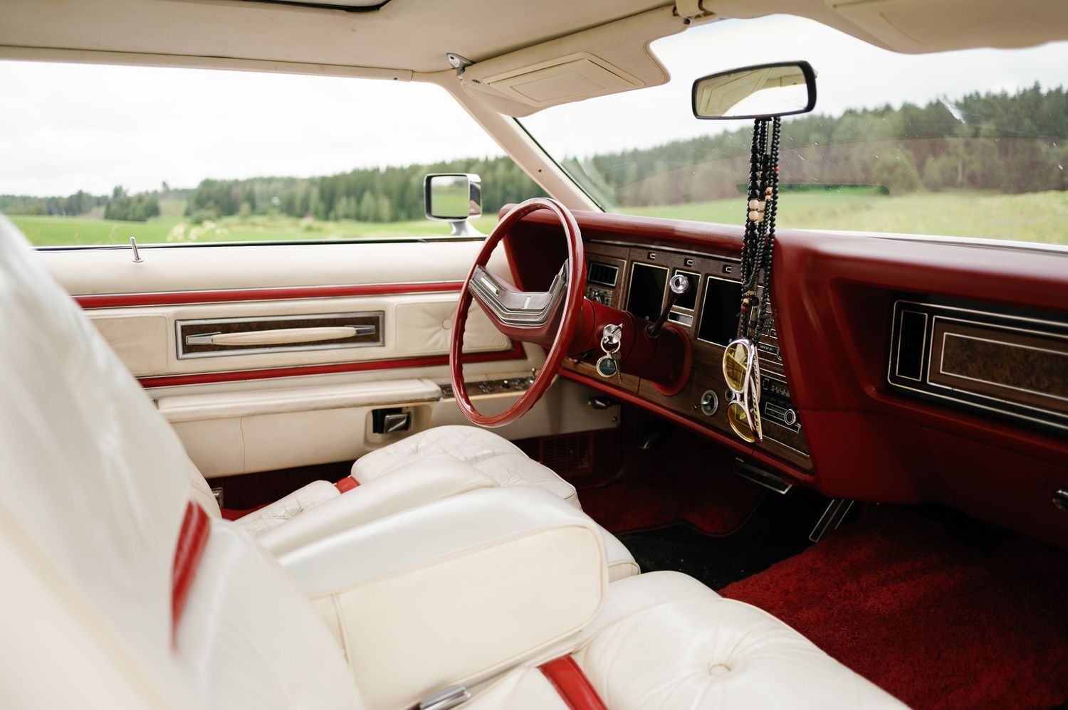 Interior view of a vintage car with white leather seats and red trim details.
