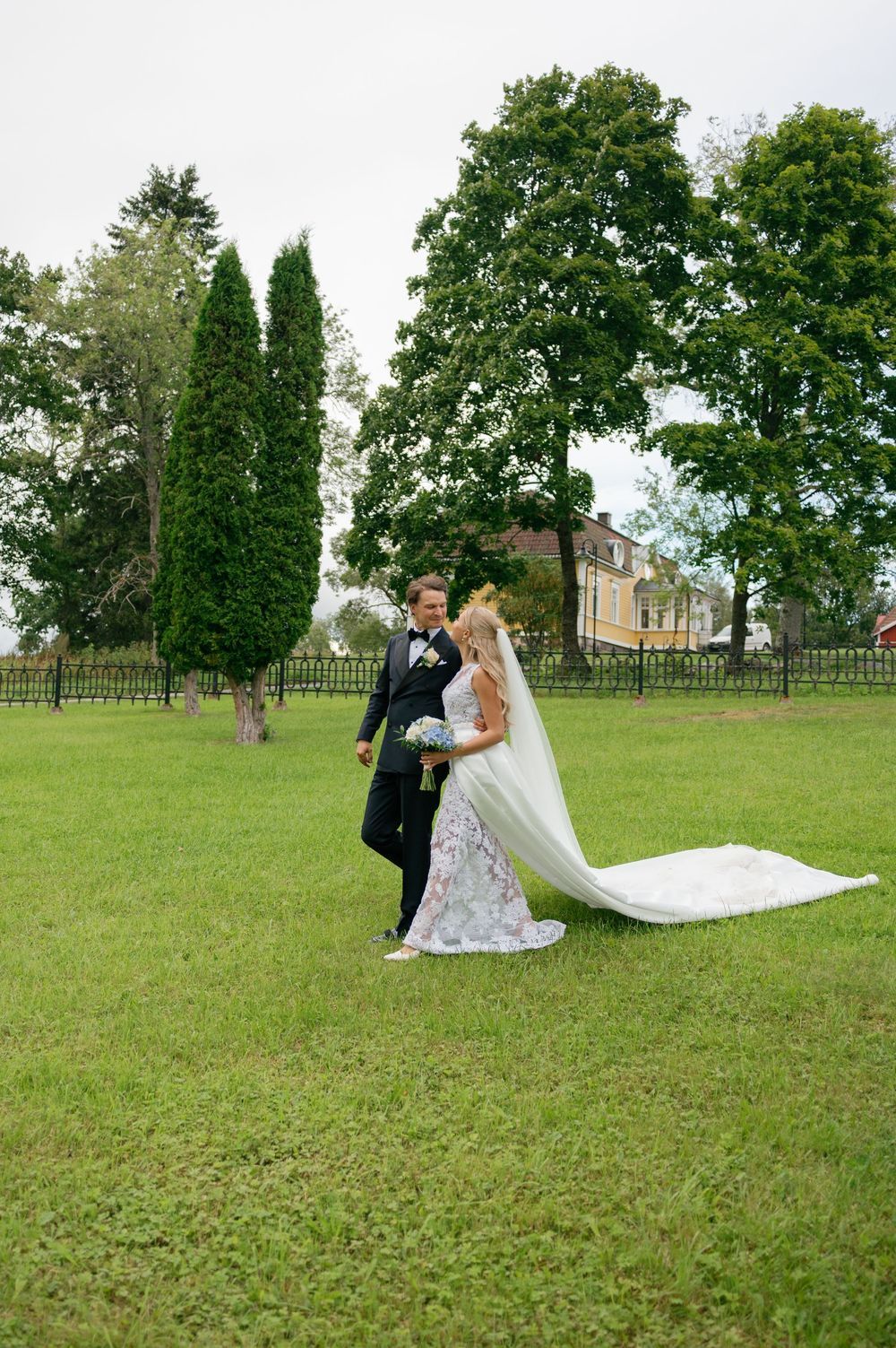 Wedding couple poses for romantic photos on a grassy lawn surrounded by trees.