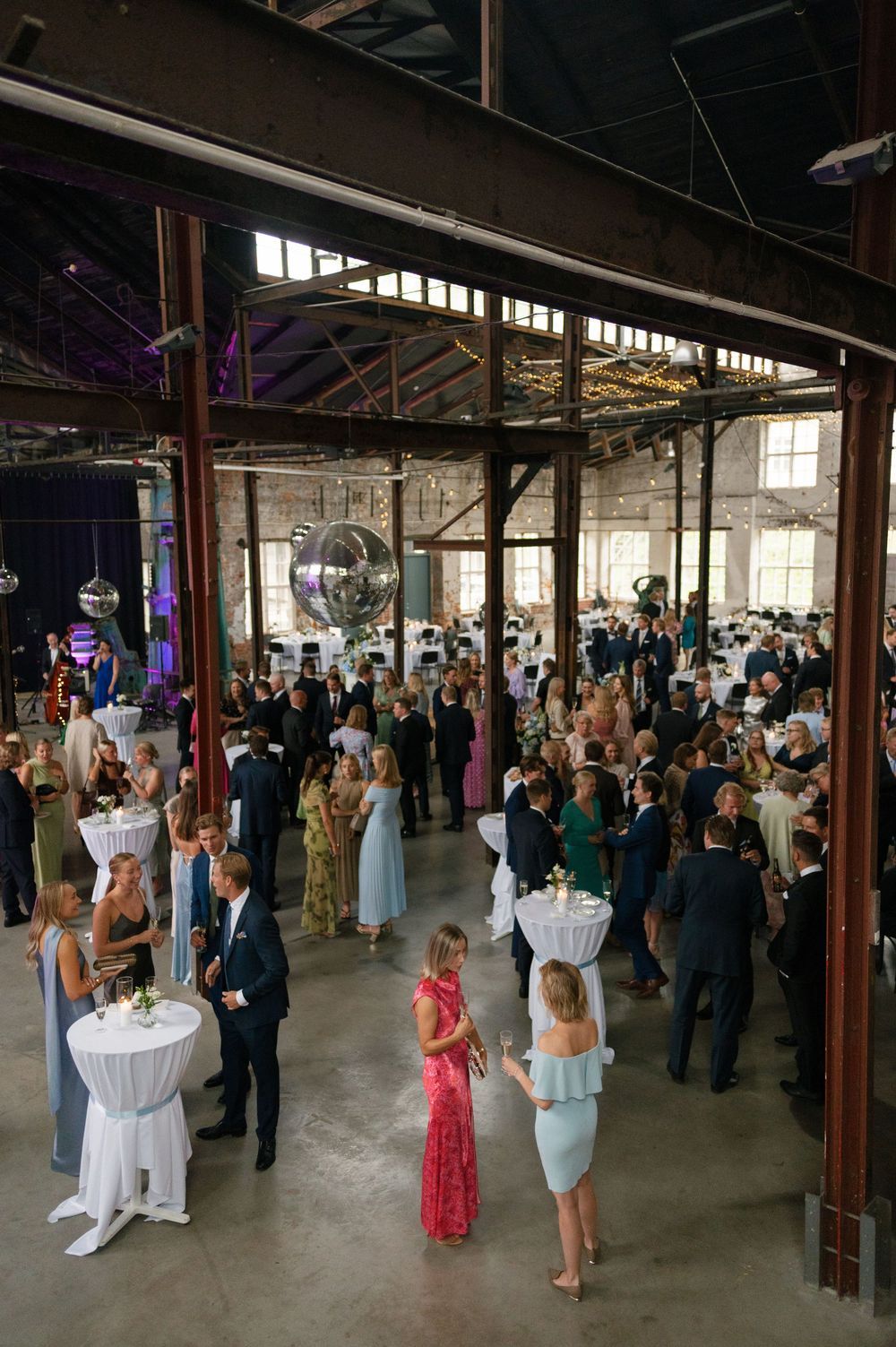 Wide view of wedding reception with guests socializing in an industrial warehouse space.
