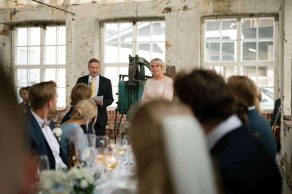 Wedding reception in a rustic industrial venue with exposed brick walls and large windows.