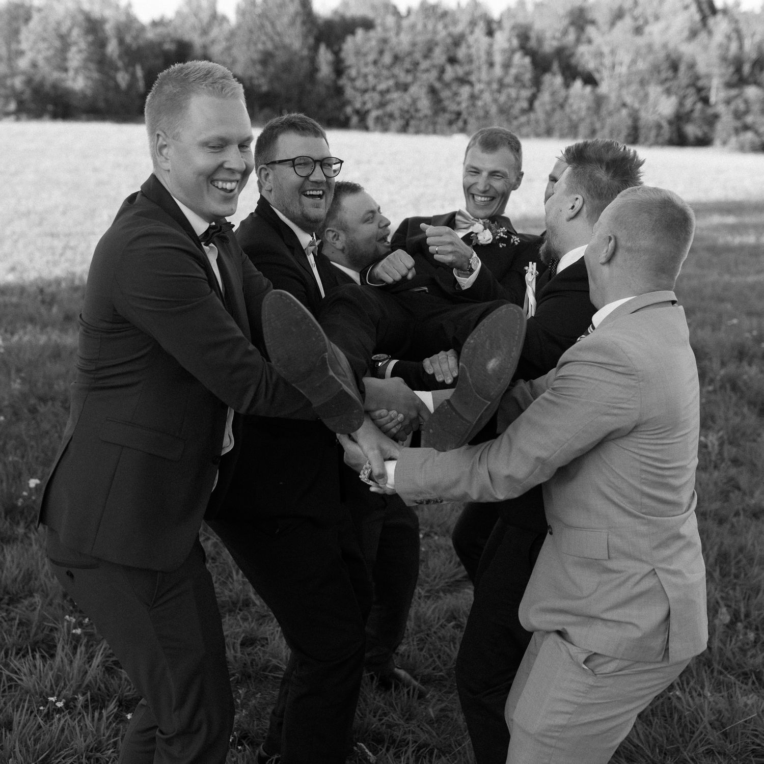 Wedding party members engage in a playful mock fight scene outdoors.