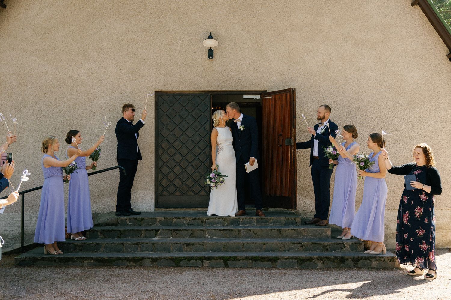 Wedding party members line up on the steps of a white chapel for photos.