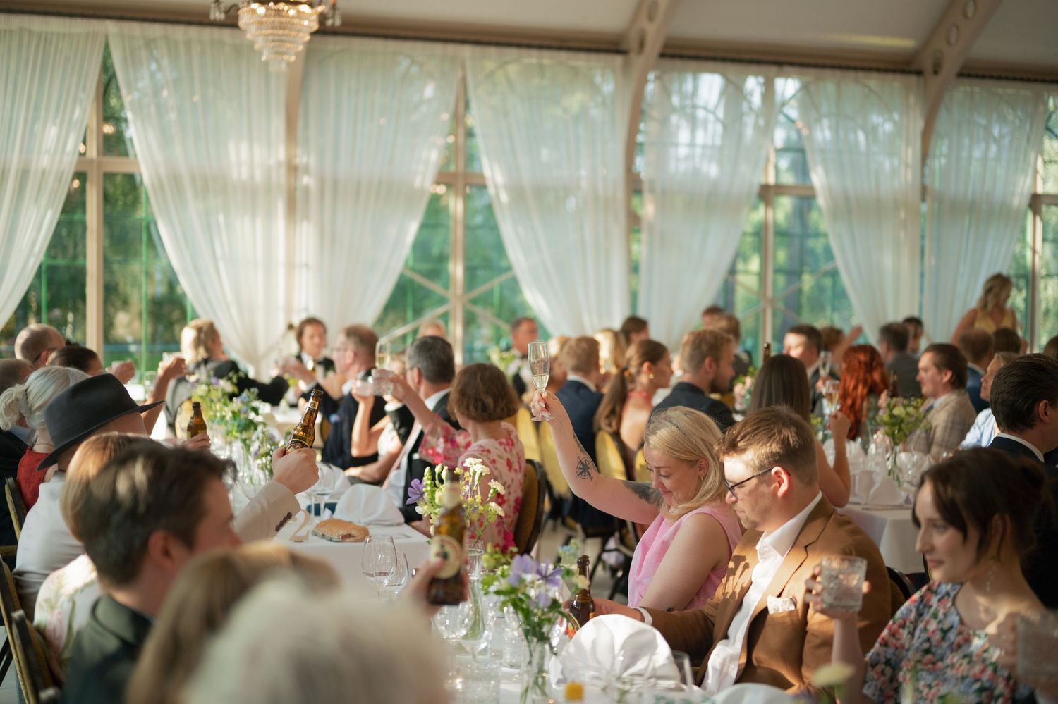 Wedding guests celebrating and raising glasses during reception dinner.
