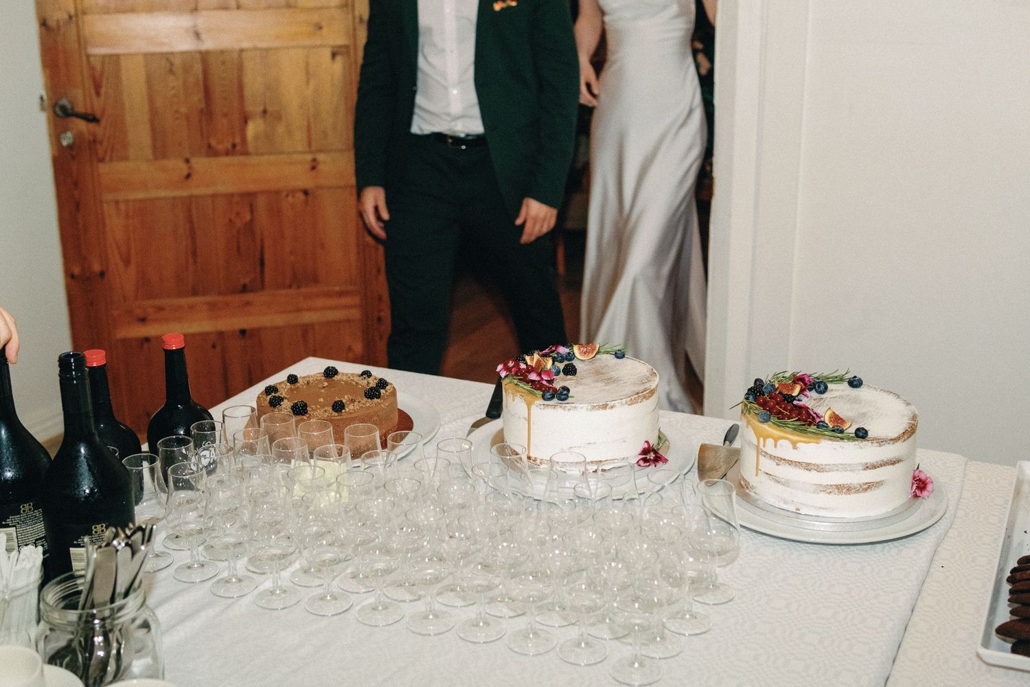 Wedding reception dessert table with elegant cakes and champagne glasses arranged on white tablecloth.