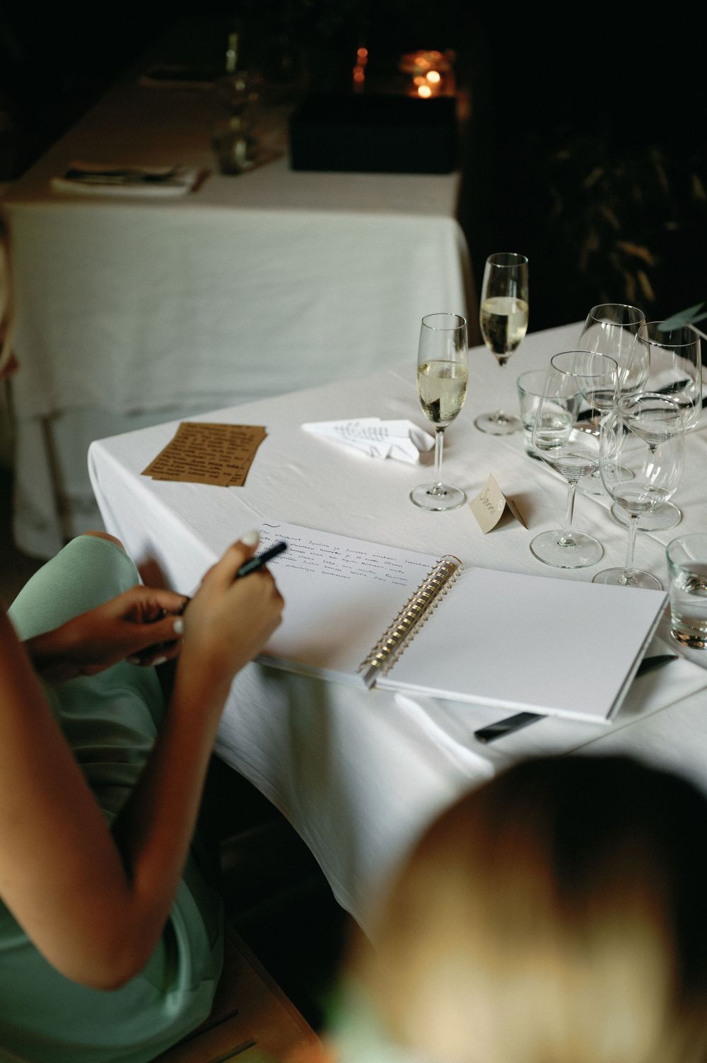 Guest signing a guestbook at an elegant table setting with wine glasses.