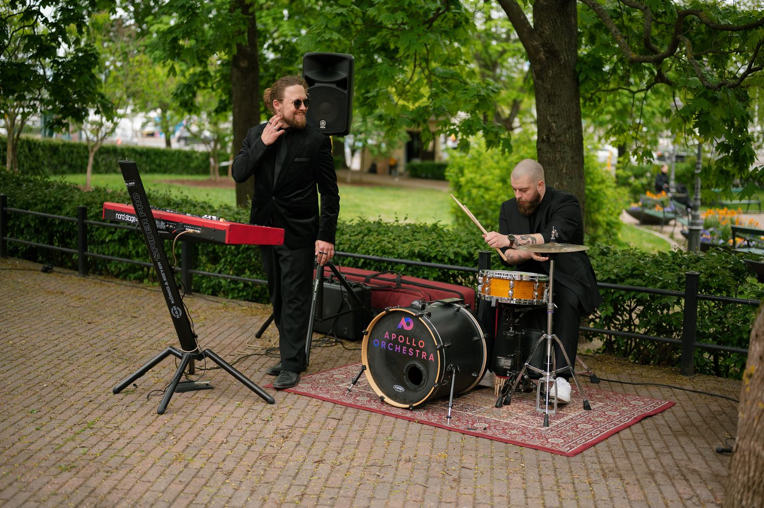 Musicians perform outdoors in a lush green park setting on a sunny afternoon.