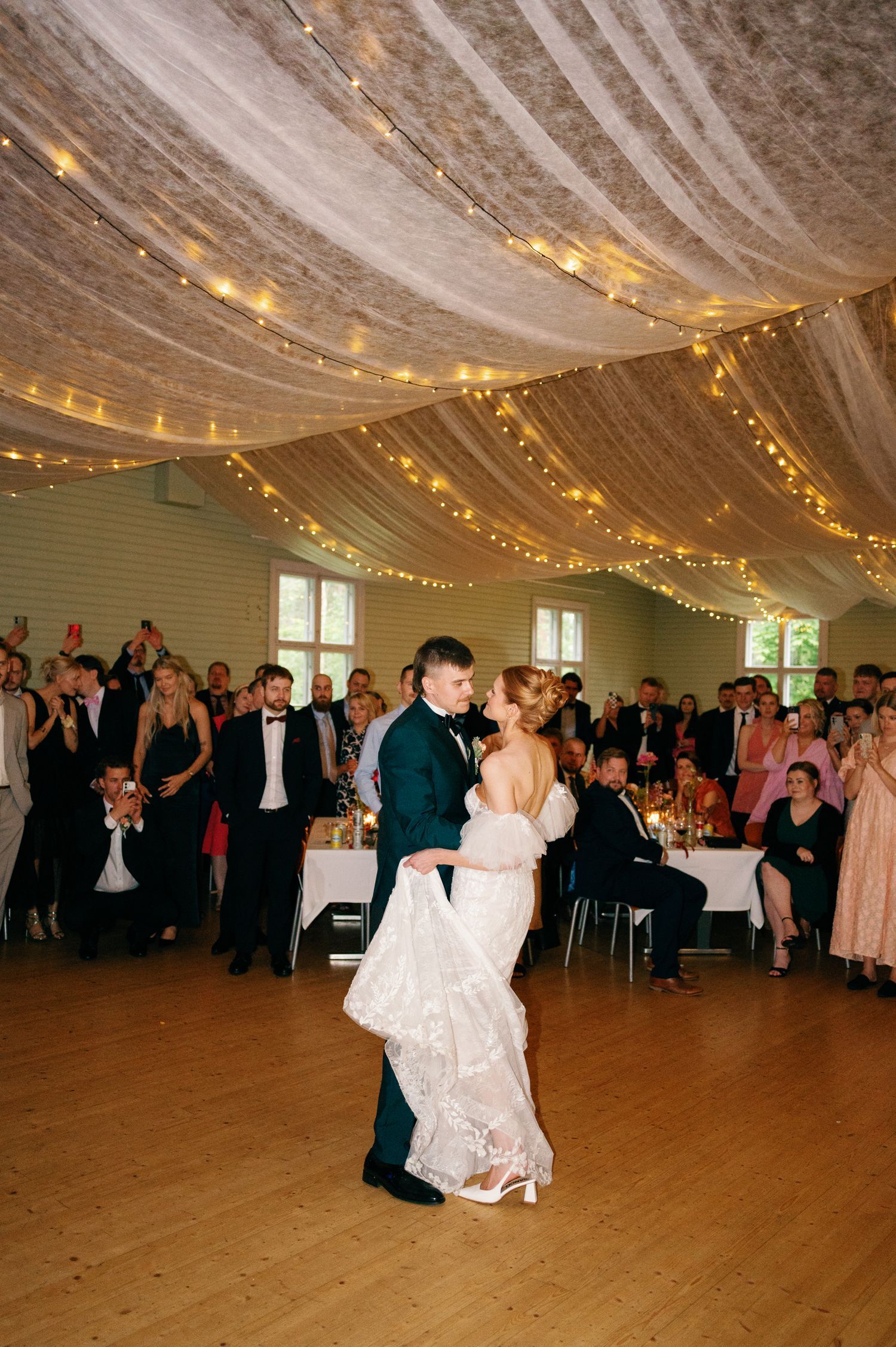 Couples dancing at a wedding reception under white fabric and twinkle light decor.