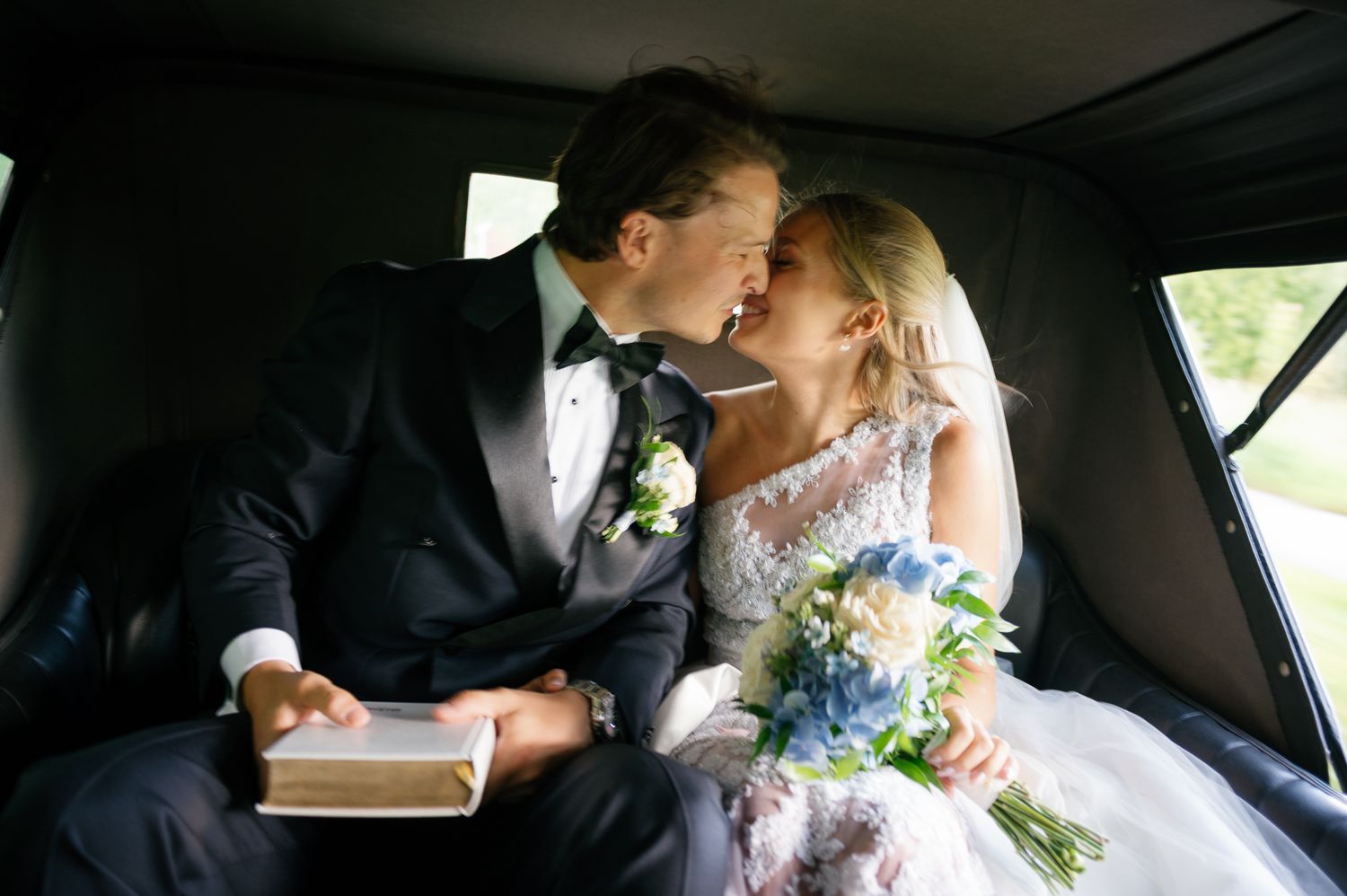 A bride and groom share an intimate moment in the back seat of a car after their wedding ceremony.