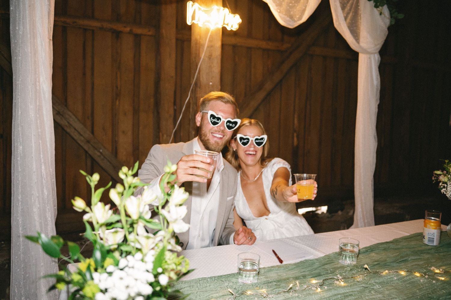 Wedding party enjoys drinks and conversation at decorated barn reception tables.