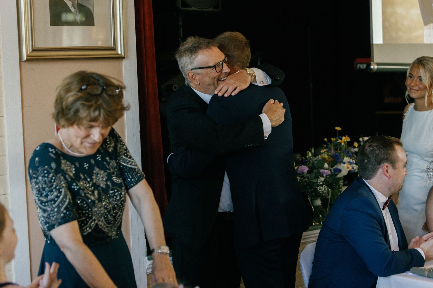 Wedding guests sharing emotional embraces during reception celebration.
