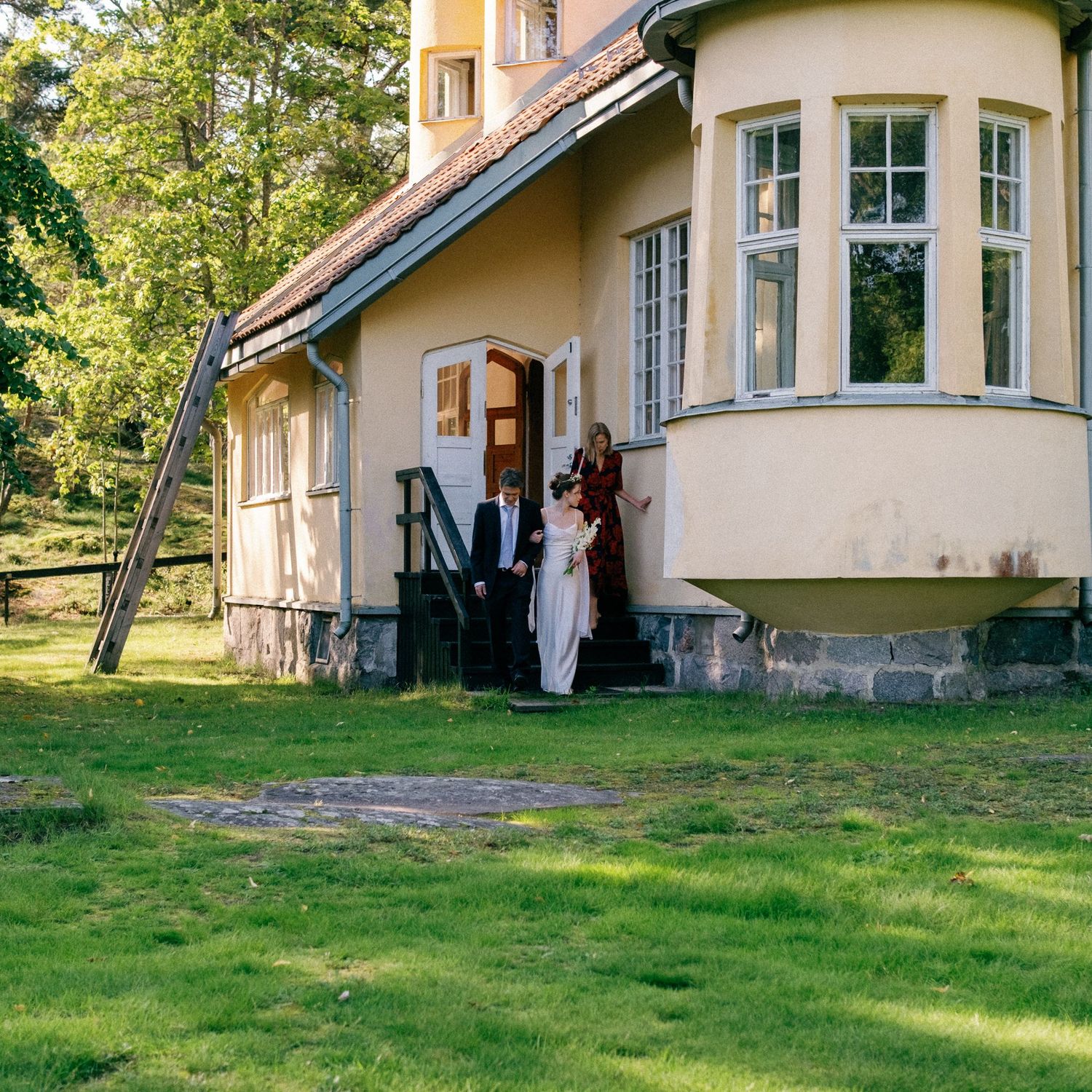 A beautiful yellow mansion with white trim sits on a grassy lawn surrounded by trees in golden sunlight.