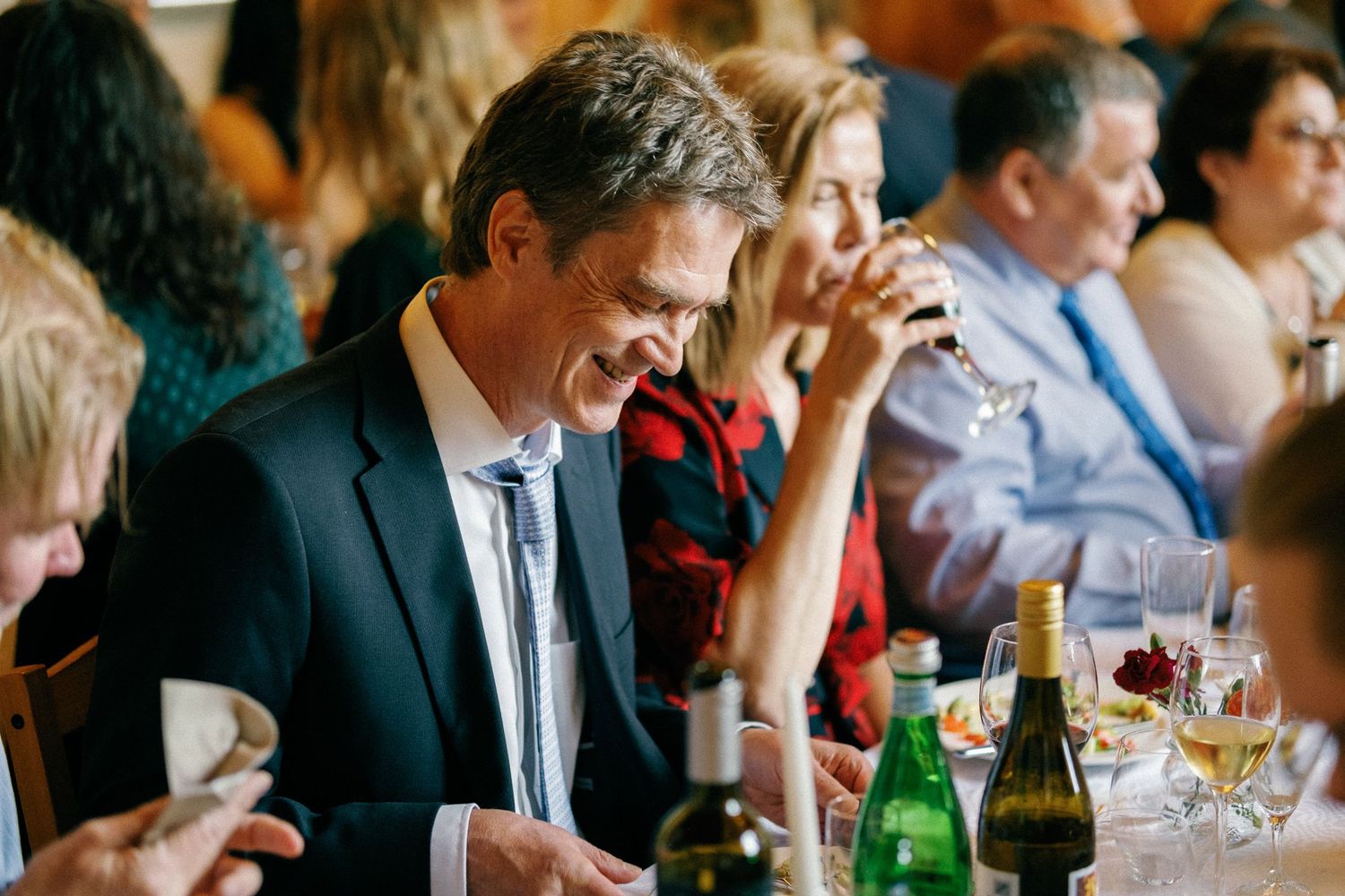 Wedding guests seated at long tables with wine bottles and casual dining settings.