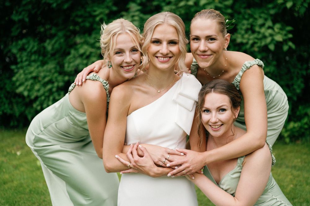 Bridesmaids in light green dresses share a joyful moment outdoors.