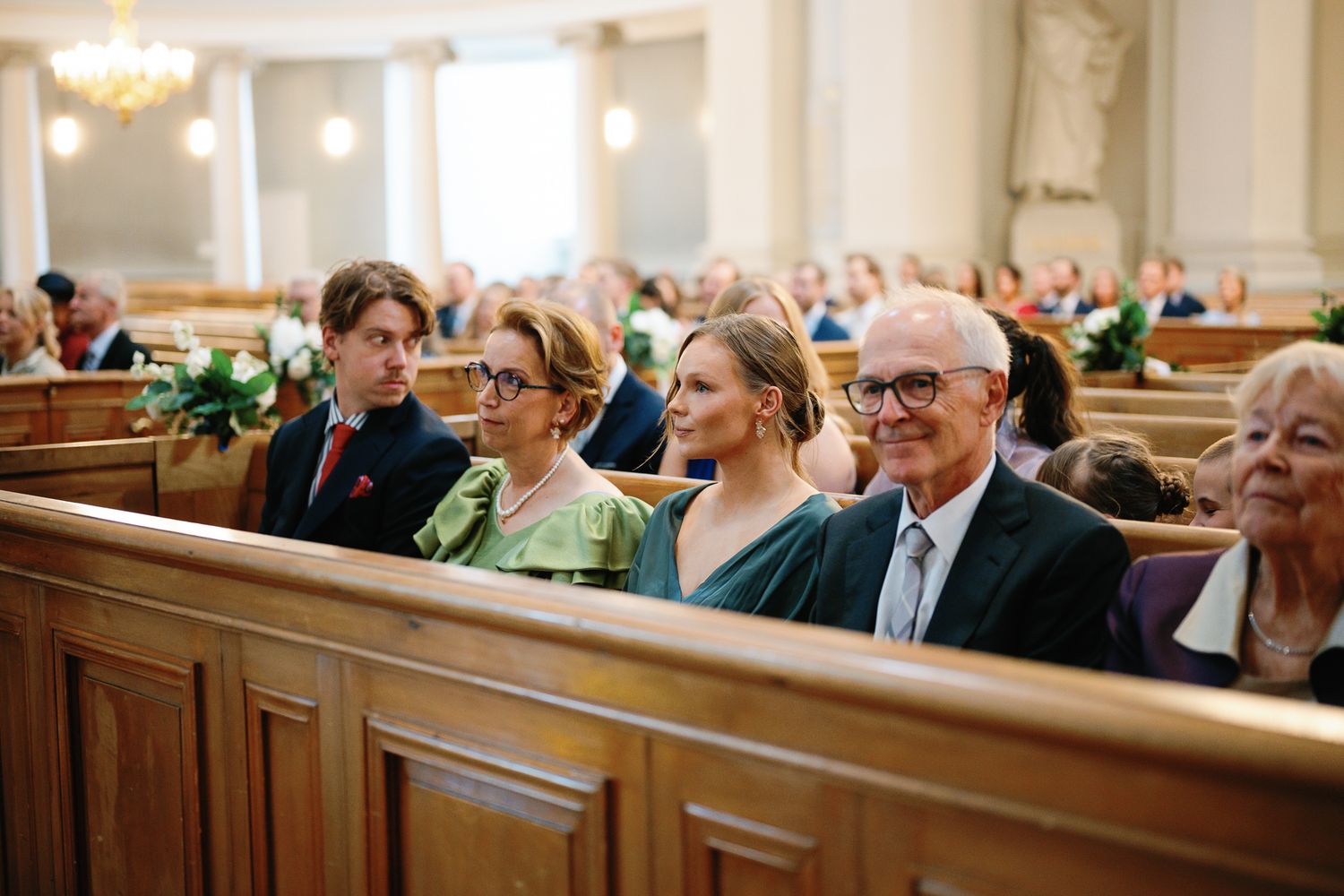 Guests smiling and seated in wooden church pews during a wedding ceremony in an elegant venue.