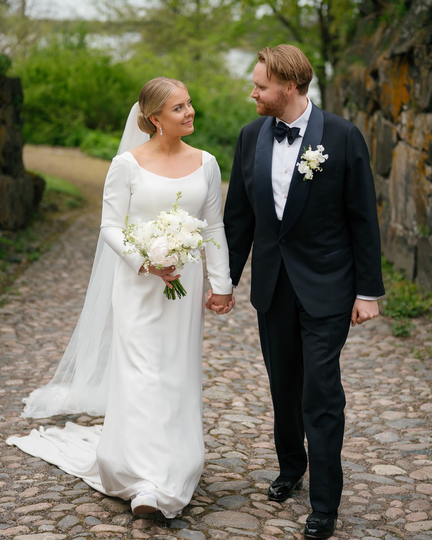 A bride and groom walk together on a cobblestone path during their wedding day.