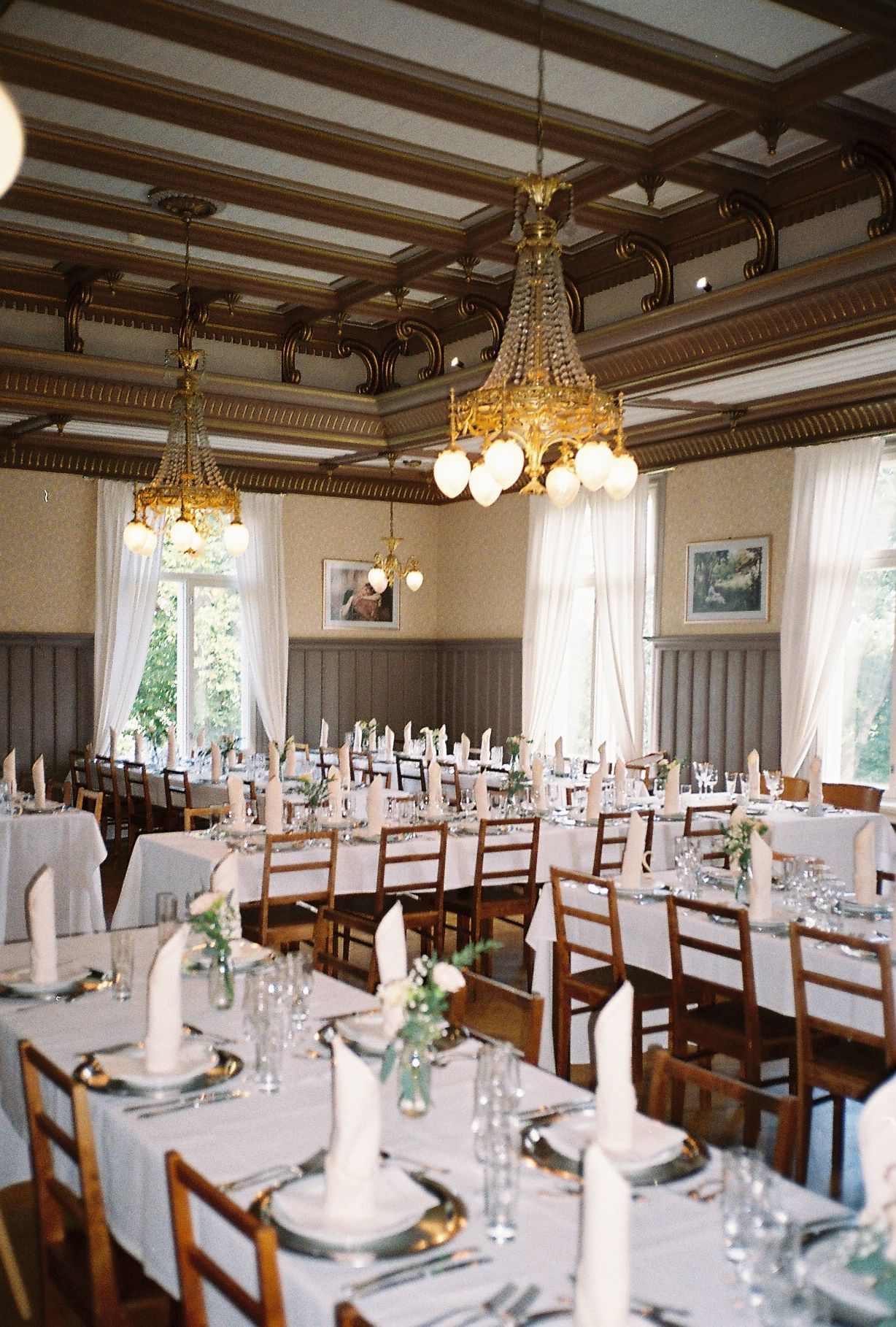 Elegant banquet hall set for wedding reception with wooden chairs and chandeliers.