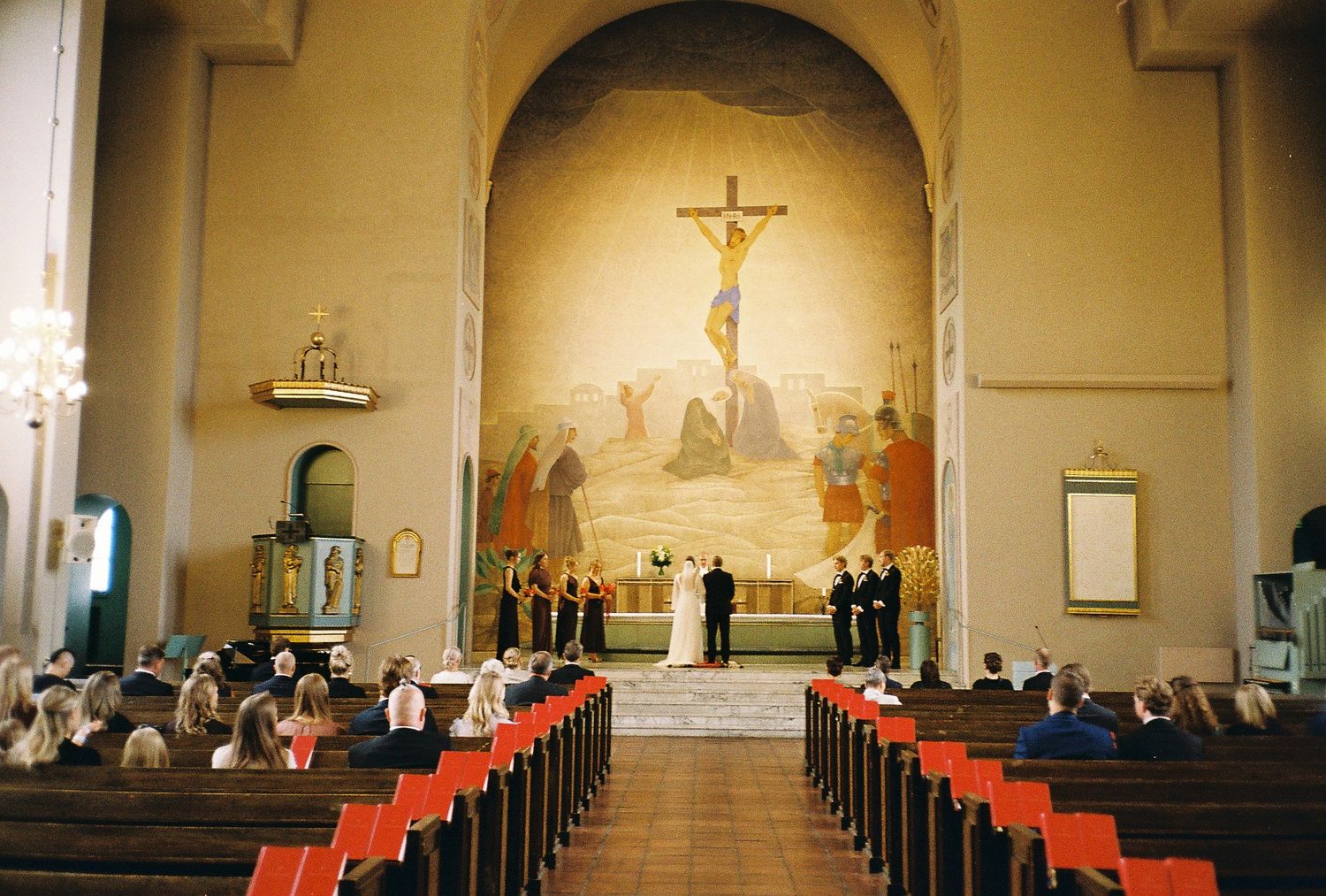 Church sanctuary with crucifixion mural and rows of wooden pews.