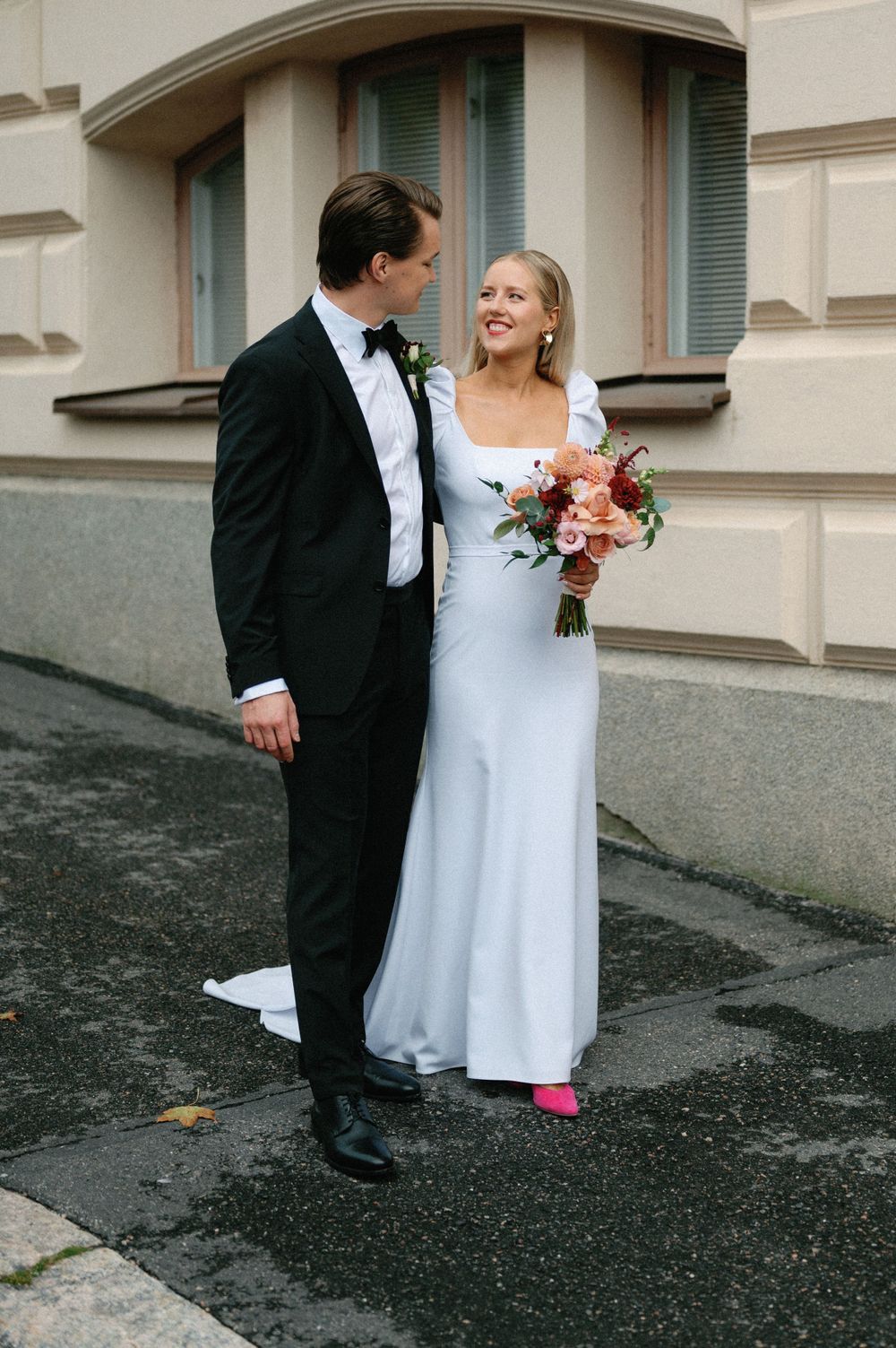 Elegant wedding couple on city street with bride in white dress and bright pink shoes.