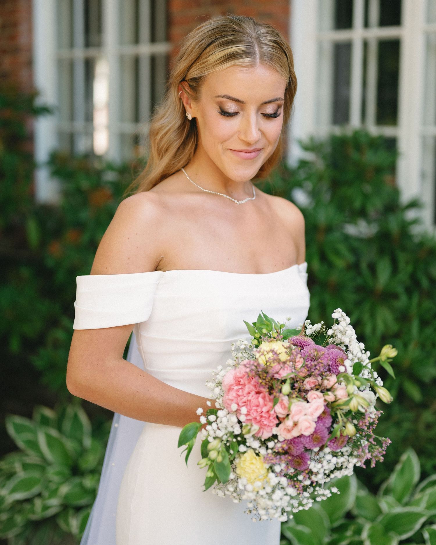 Elegant bridal bouquet featuring pink, purple and white flowers against a white dress.