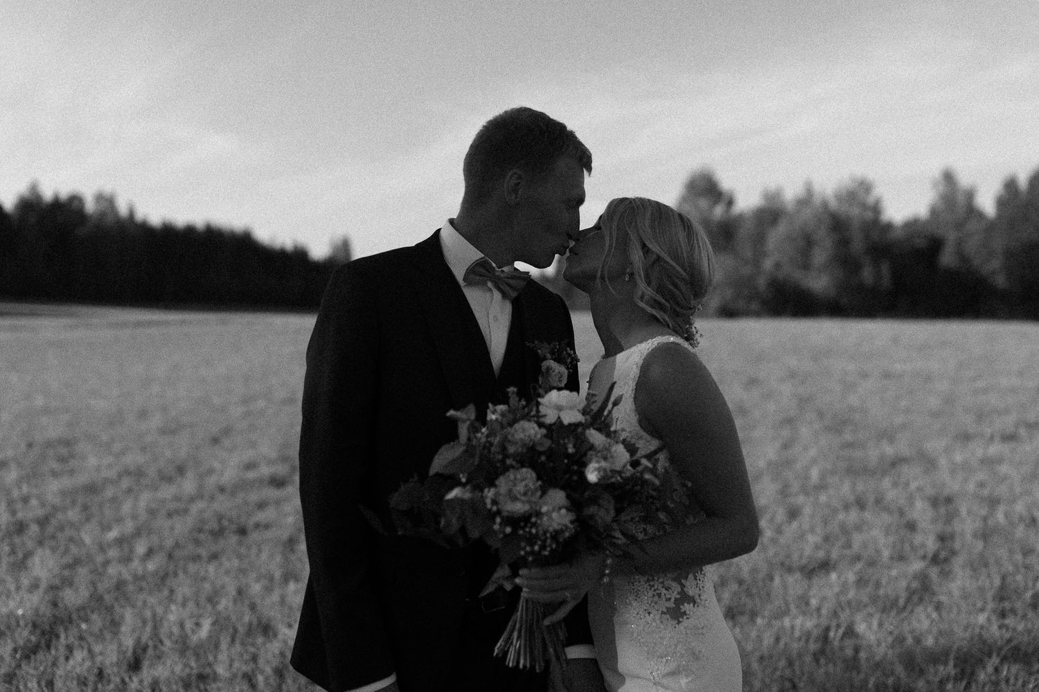 Romantic wedding couple embracing in an outdoor field during golden hour.