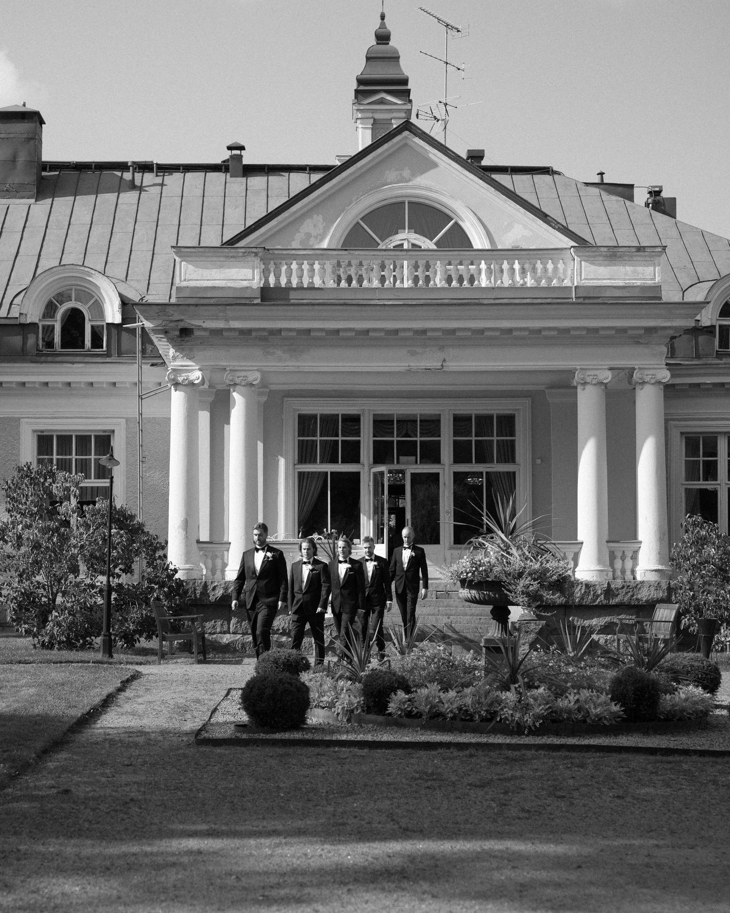 Black and white photograph of a classic white mansion with columned entrance and formal landscaping.