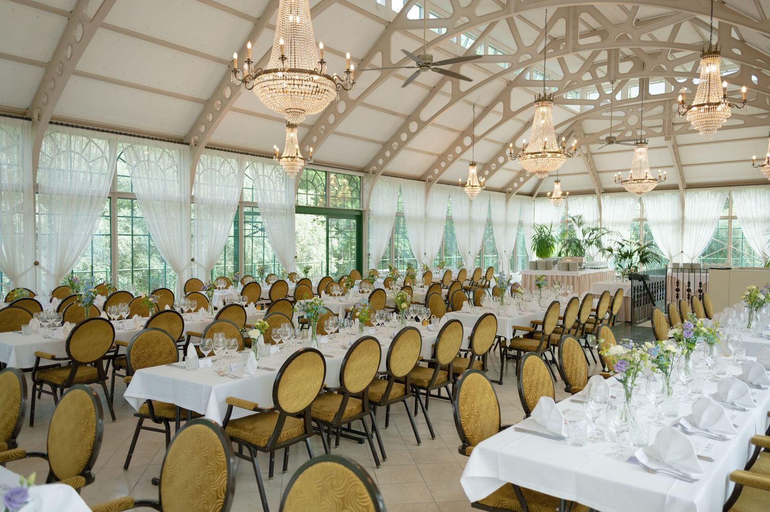Large elegant wedding reception hall with crystal chandeliers and rows of tables set for dinner service.