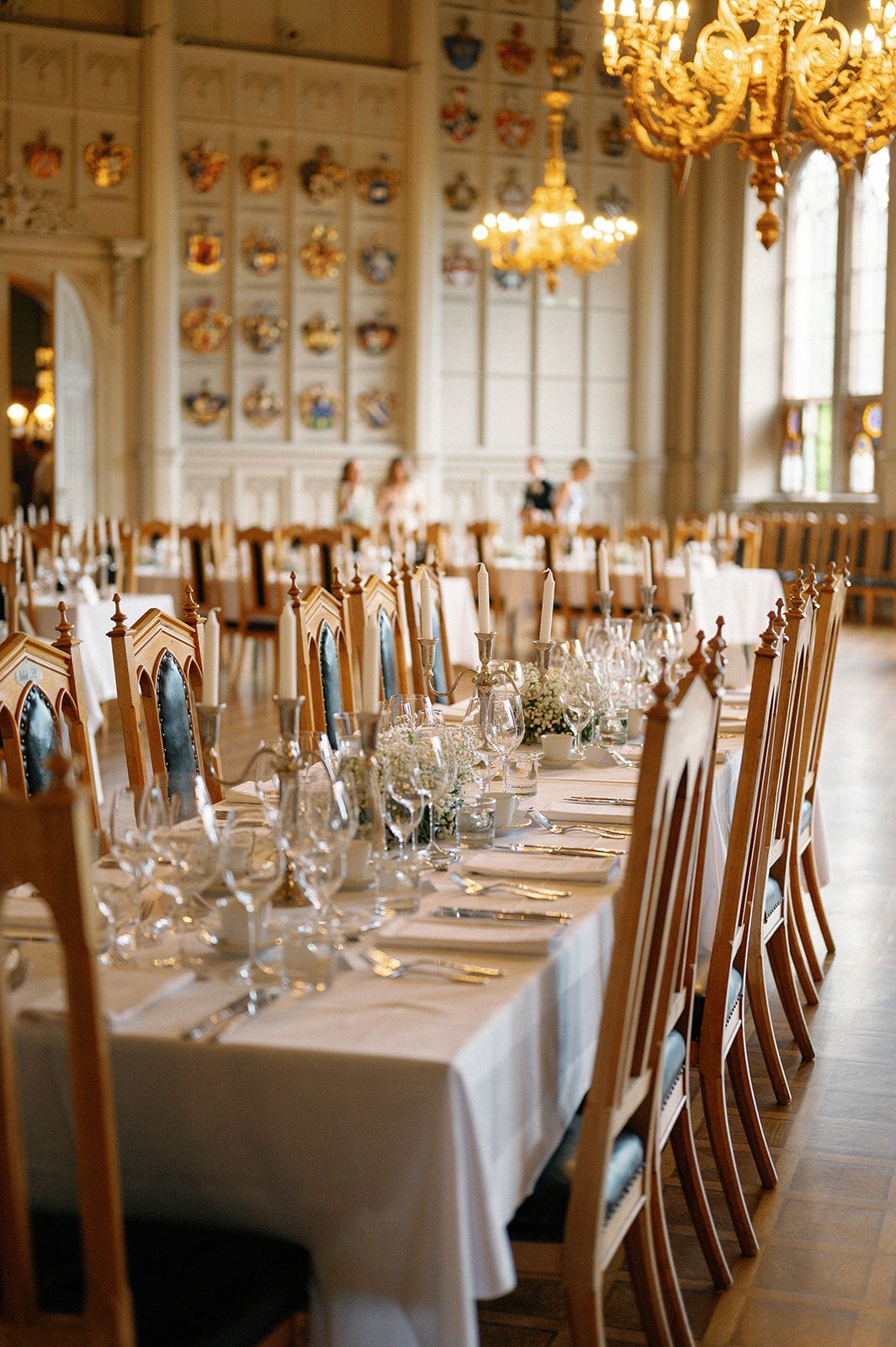 Formal dining hall with ornate chandeliers and tables set with fine glassware.