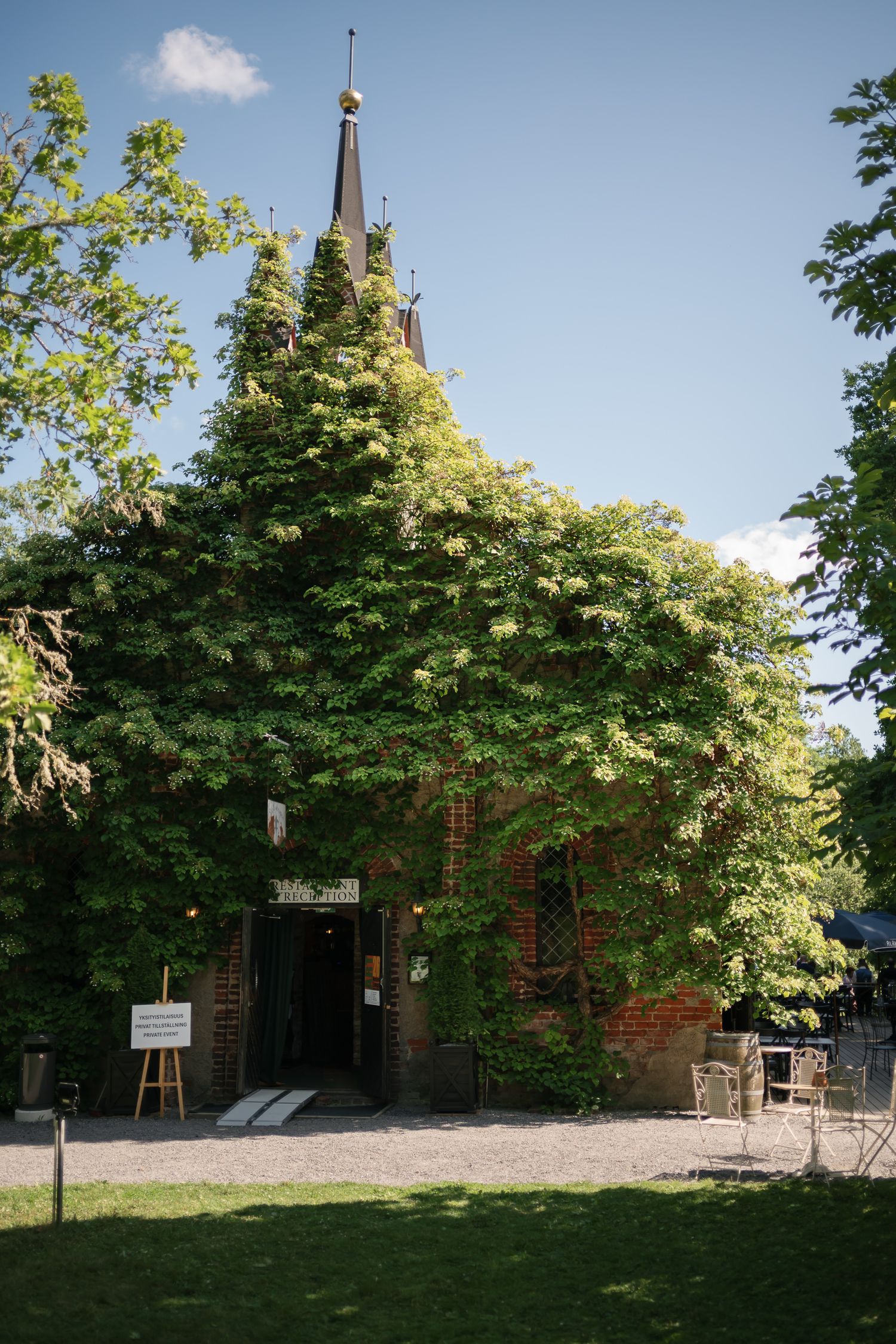 Ivy-covered brick church with a golden spire surrounded by lush green trees on a sunny day.