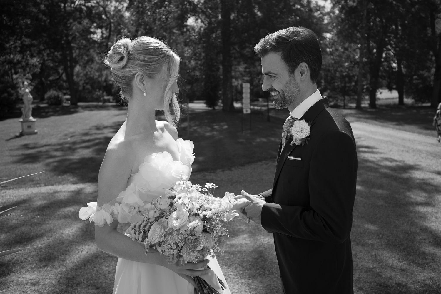 Black and white photo of a groom reading vows to his bride holding a bouquet outdoors at a wedding ceremony.