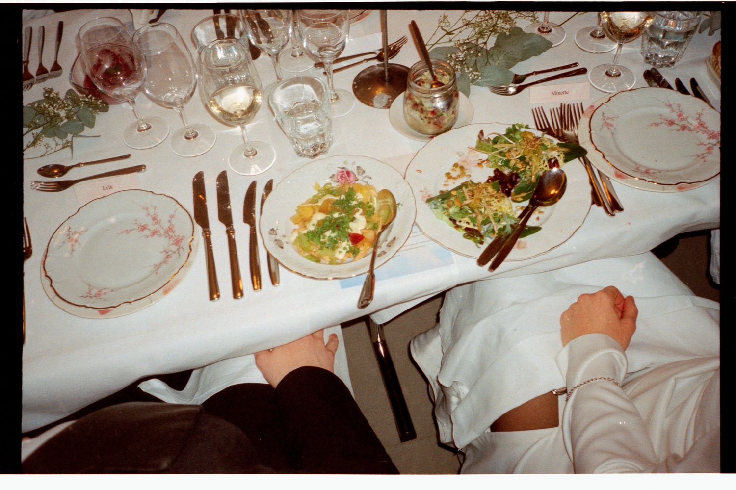 Elegant formal dinner table set with fine china, crystal glasses, and plated salads on a white linen tablecloth.