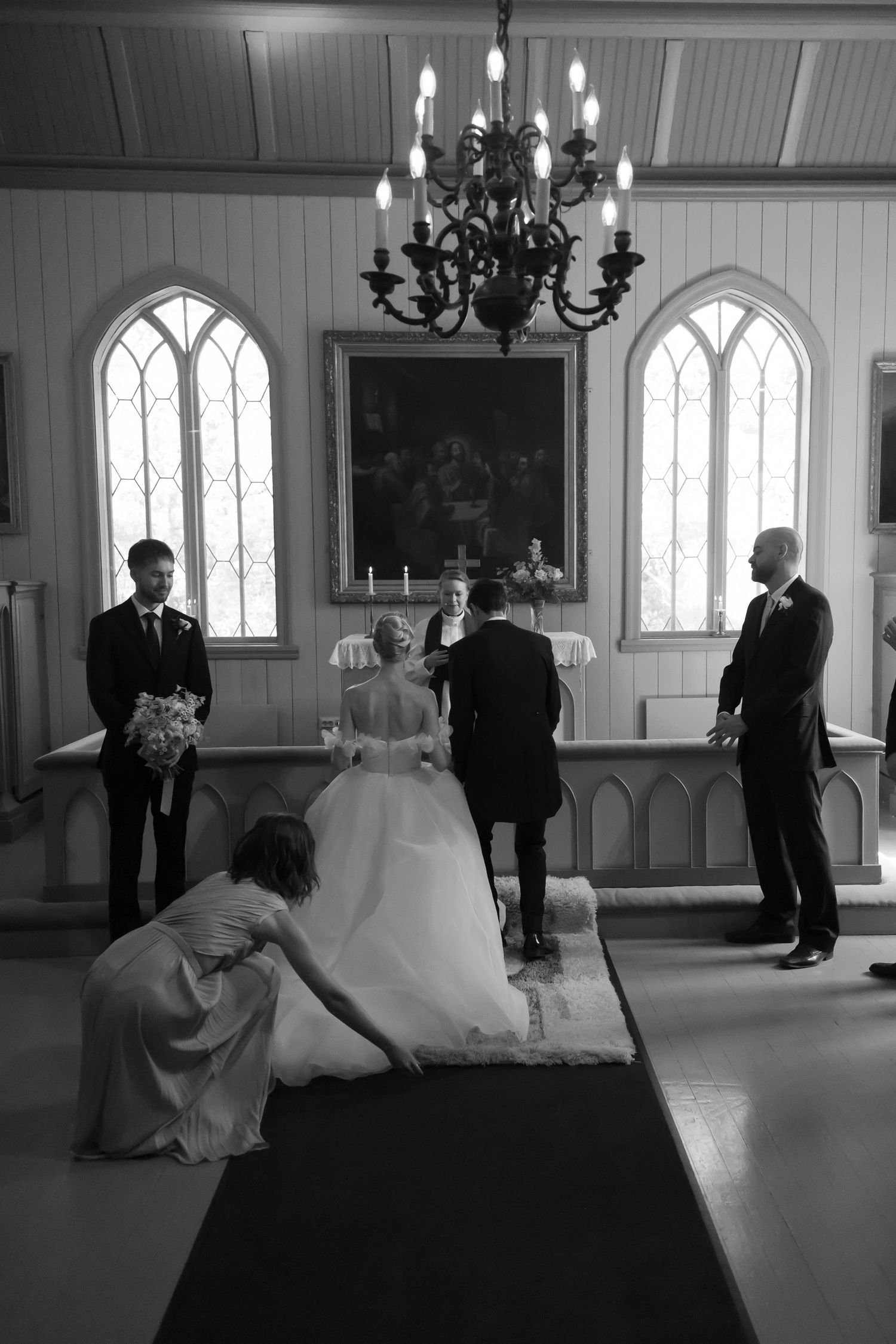 Black and white photo of a wedding ceremony in a church, bride in gown with attendants near the altar.