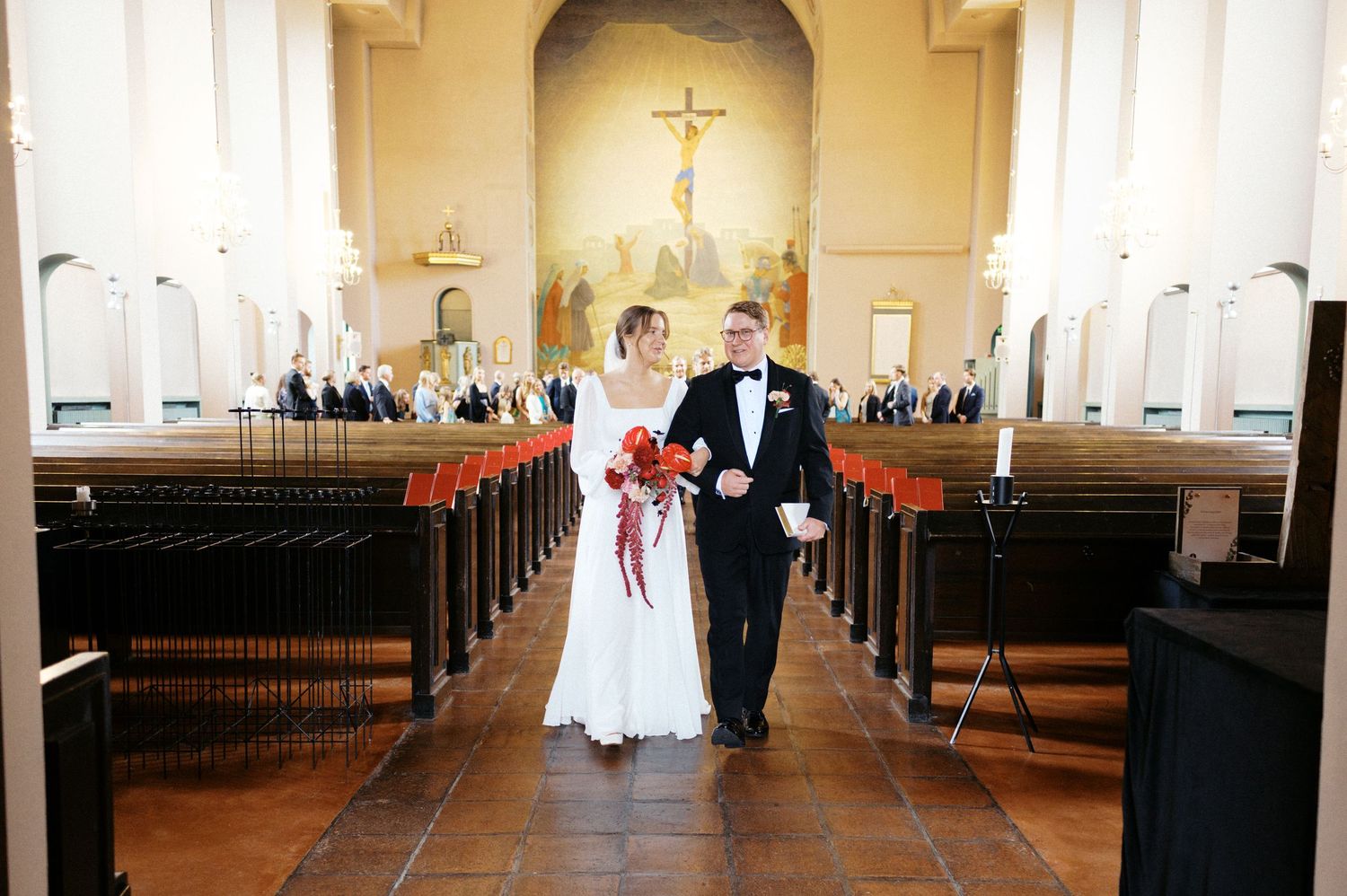 A wedding ceremony takes place in a traditional church sanctuary with wooden pews and arched ceilings.