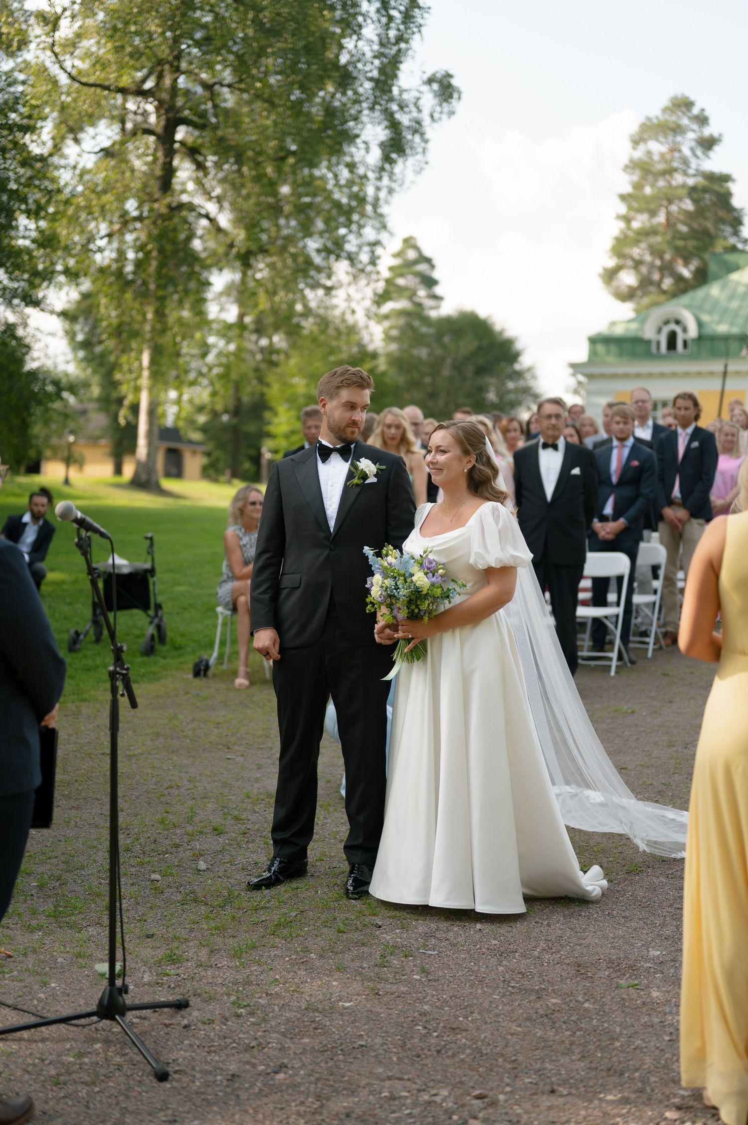 Wedding ceremony processional takes place on gravel path with mansion backdrop.