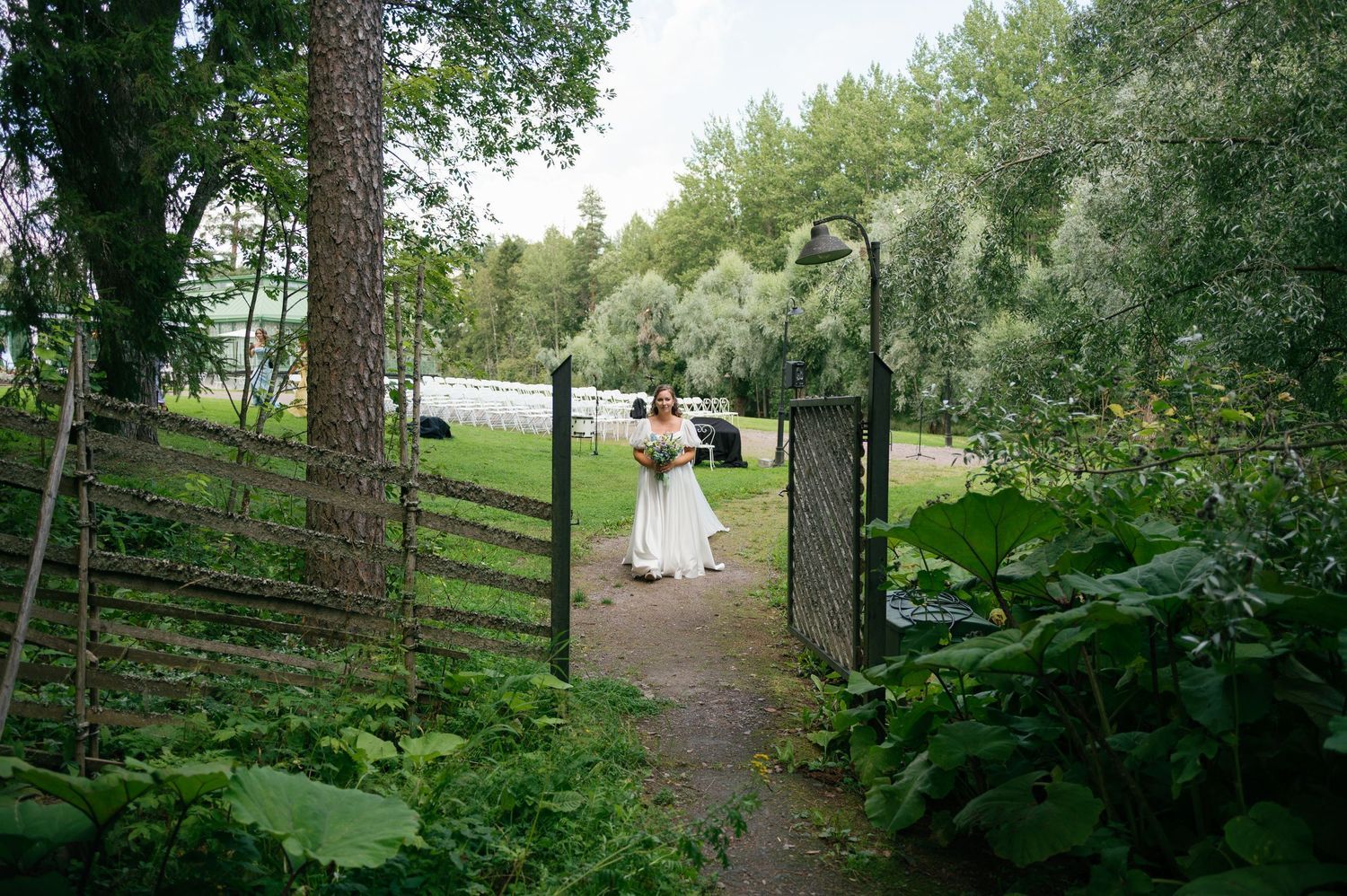 A couple walks through a rustic garden gate surrounded by verdant foliage on their wedding day.