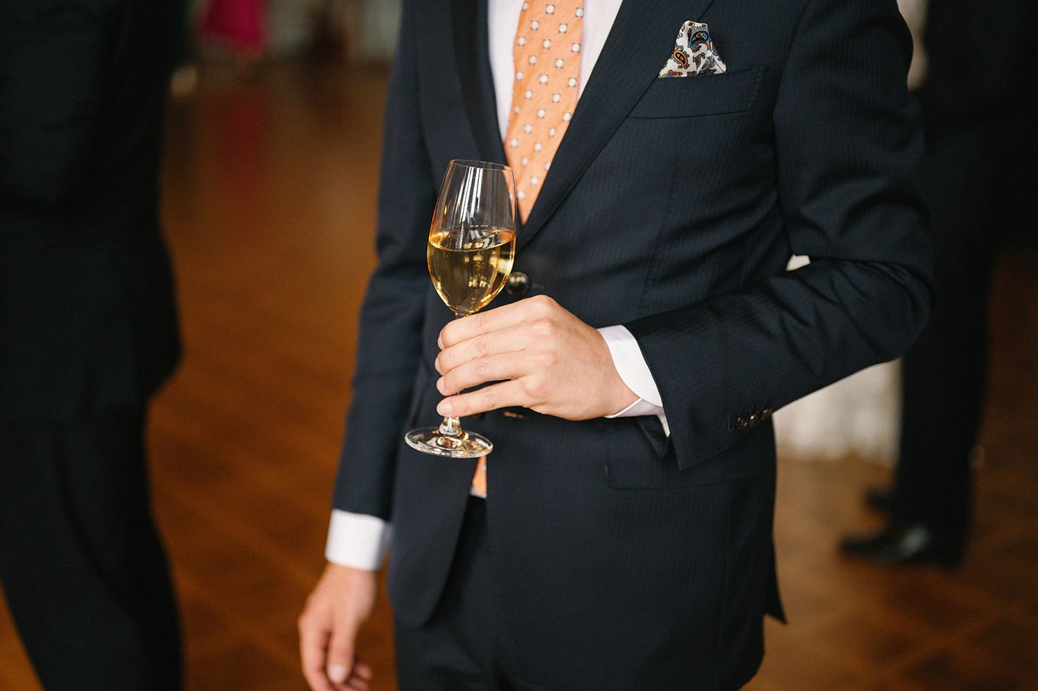 Formal event attendees in dark suits holding champagne glasses.