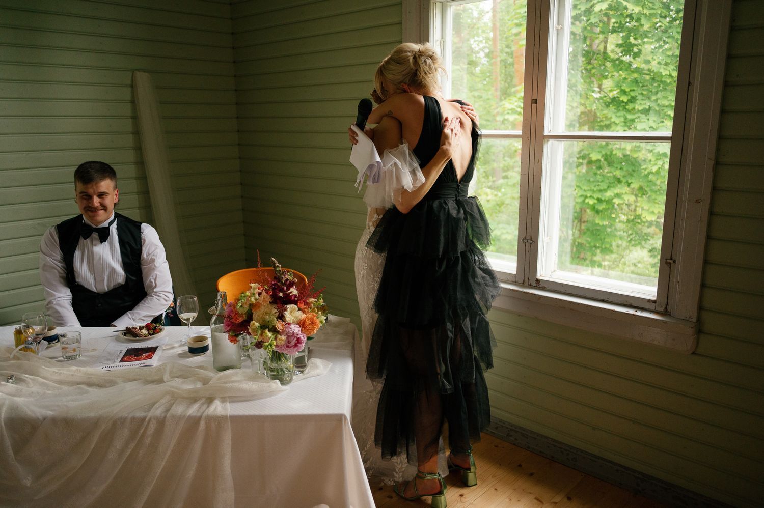 A couple shares a dance in a sunlit room with a decorated table and floral centerpiece.