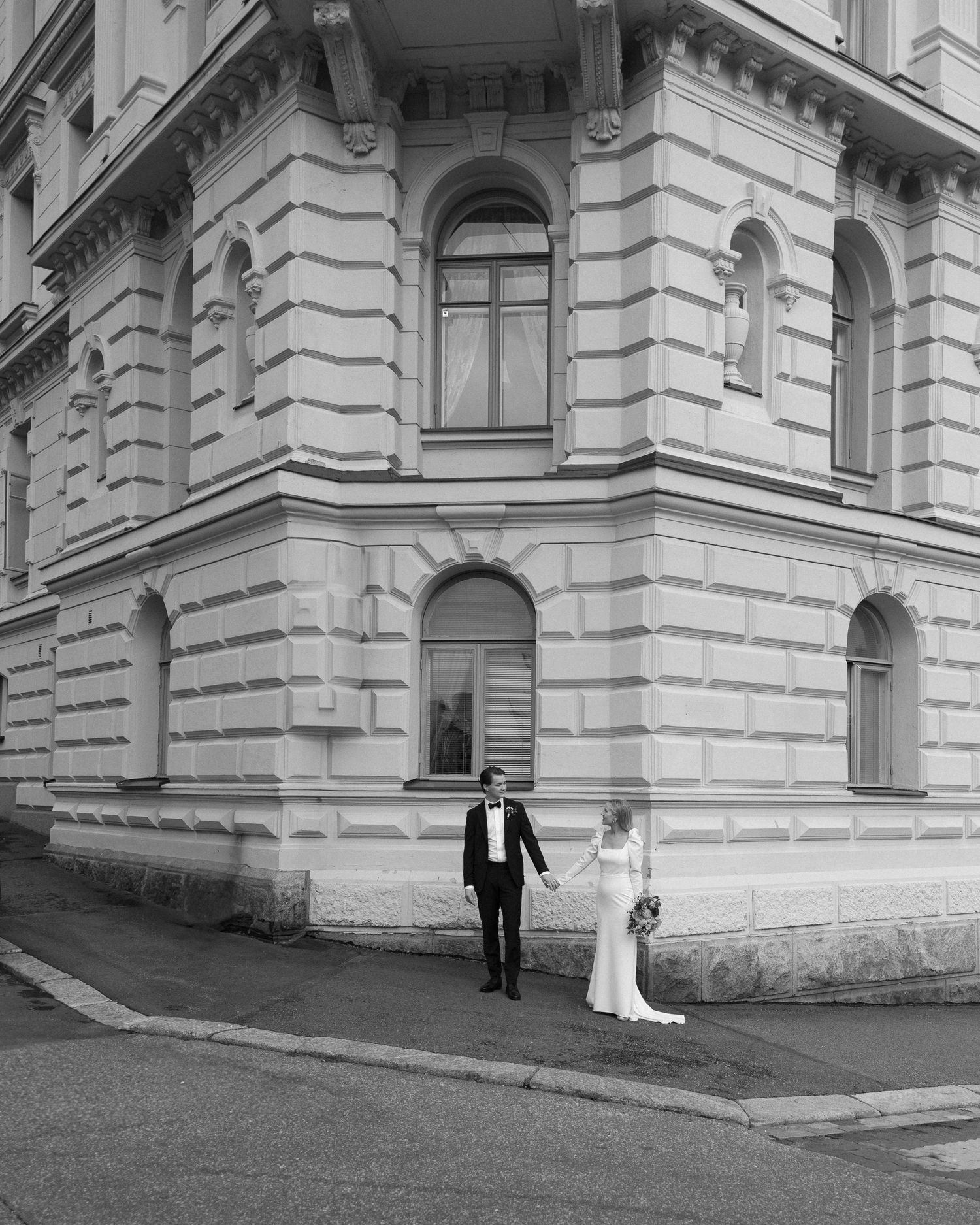 A black and white photo series showing a bride and groom walking along an ornate classical building exterior.