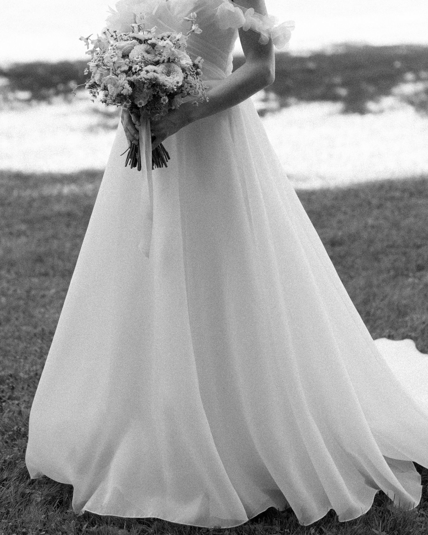 Bride in elegant white ball gown wedding dress holding floral bouquet, black and white photo.
