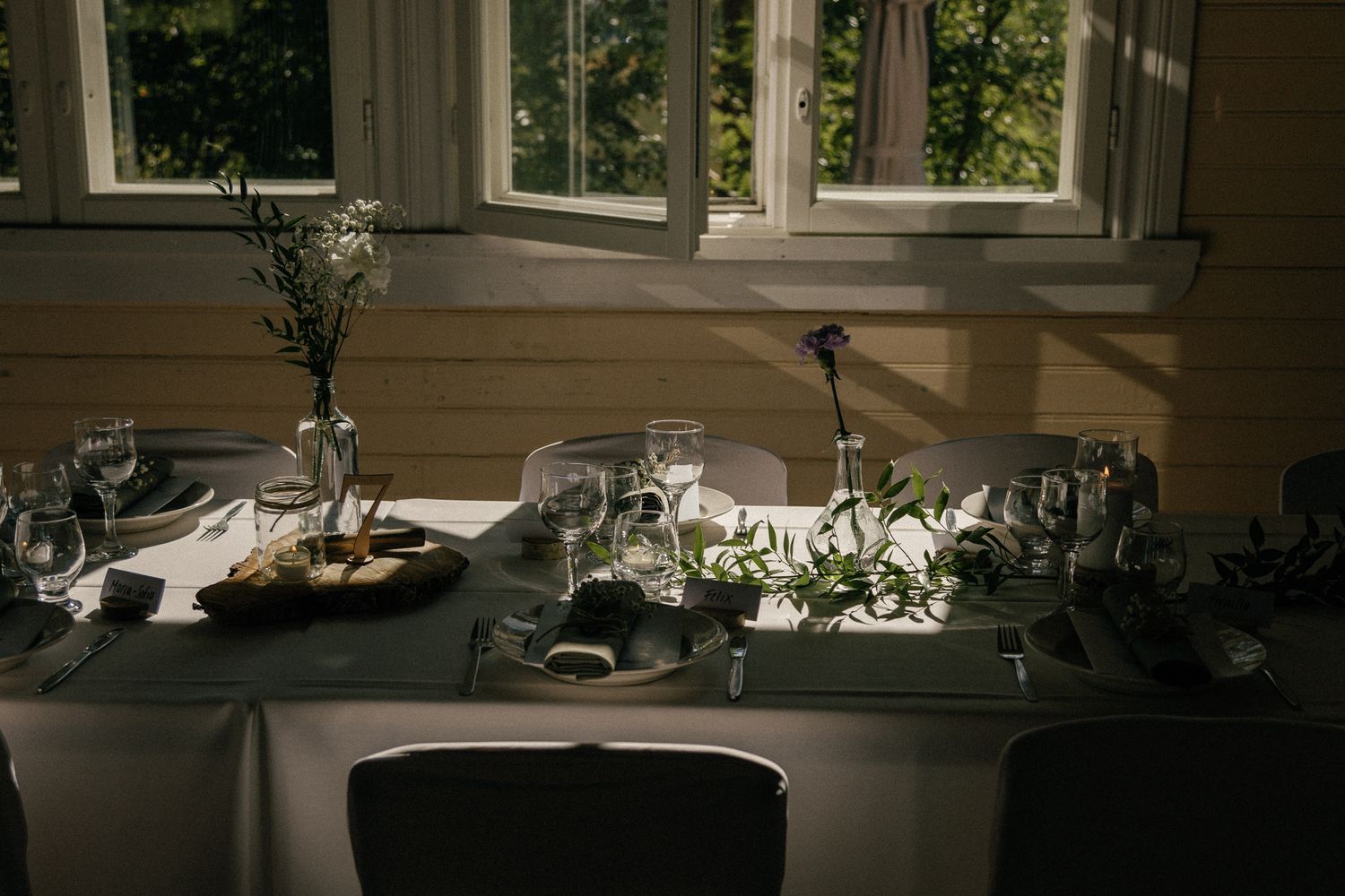 An elegant table setting with wine glasses and place settings by a sunlit window.